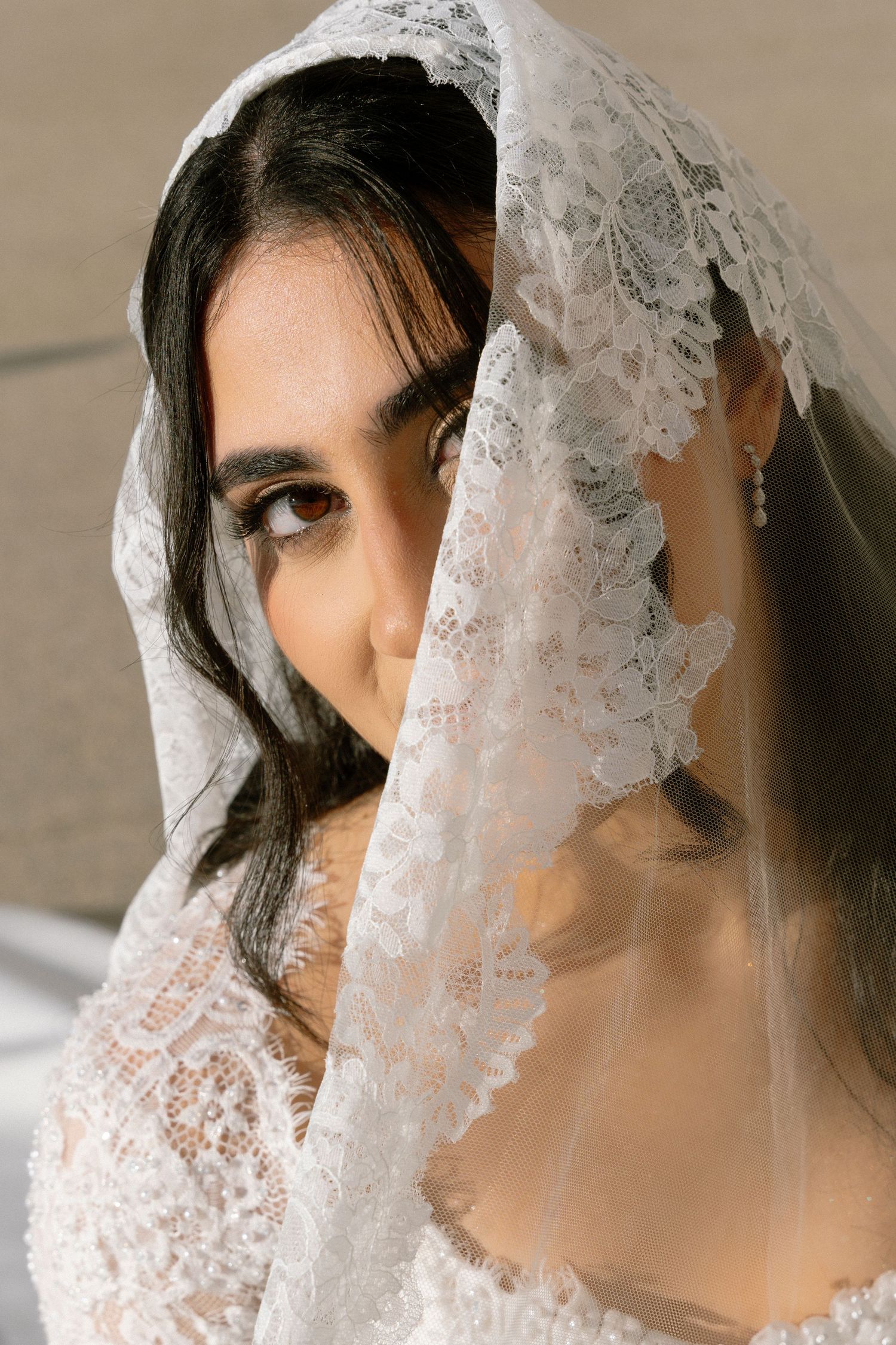A bride wearing a delicate lace veil and white wedding dress poses in a series of romantic portrait shots.