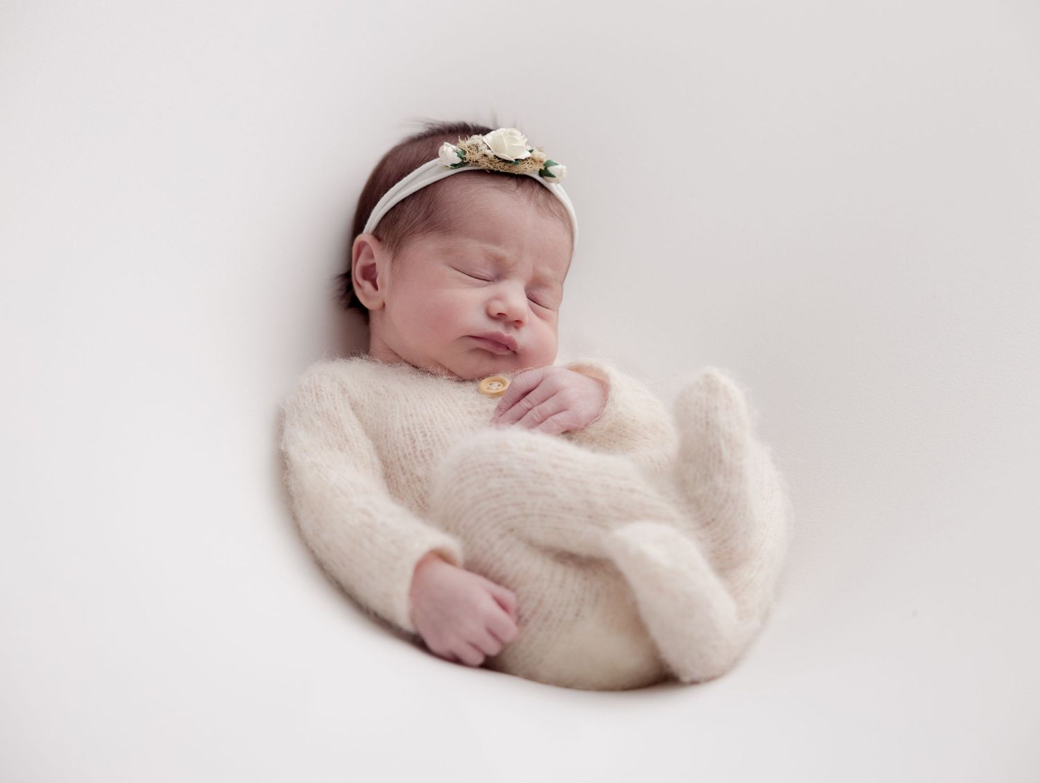 A sleeping newborn baby wrapped in soft white fabric against a light backdrop.