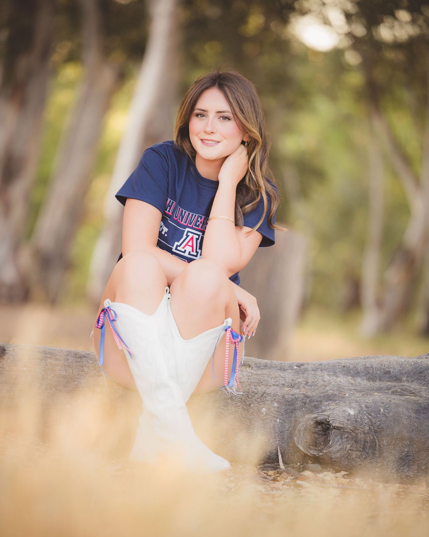 Young woman in University of Arizona shirt and white cowboy boots posing outdoors in golden field.