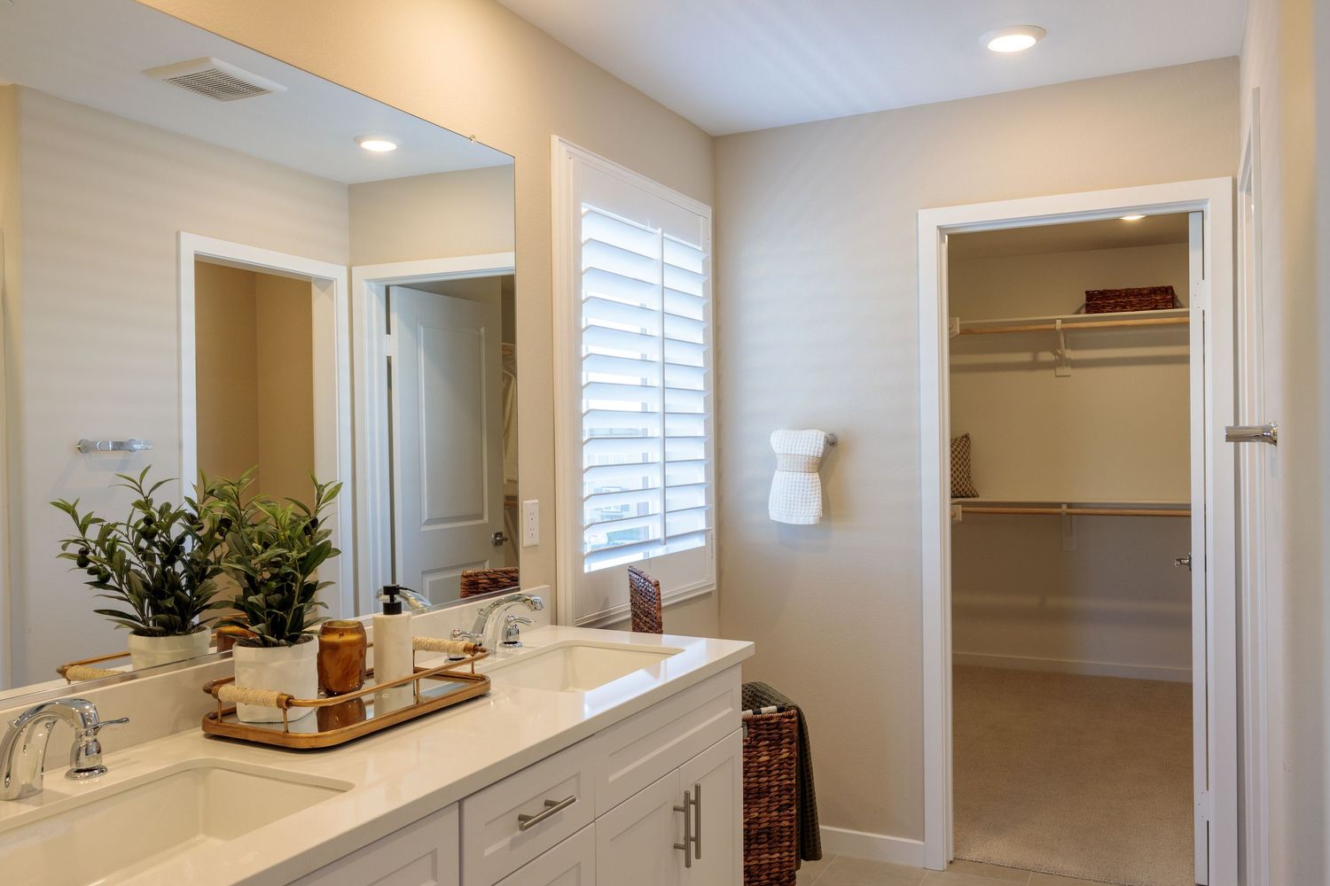 Modern bathroom interior with white cabinets, dual sinks, plantation shutters and walk-in closet entrance.