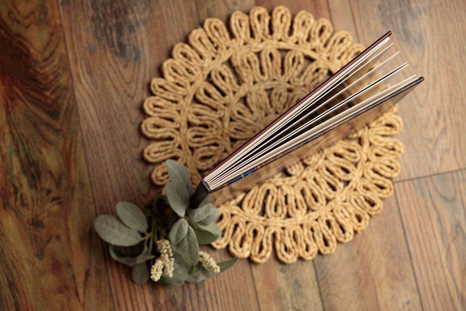 Decorative woven jute placemats arranged on a rustic wooden table surface with eucalyptus sprigs.