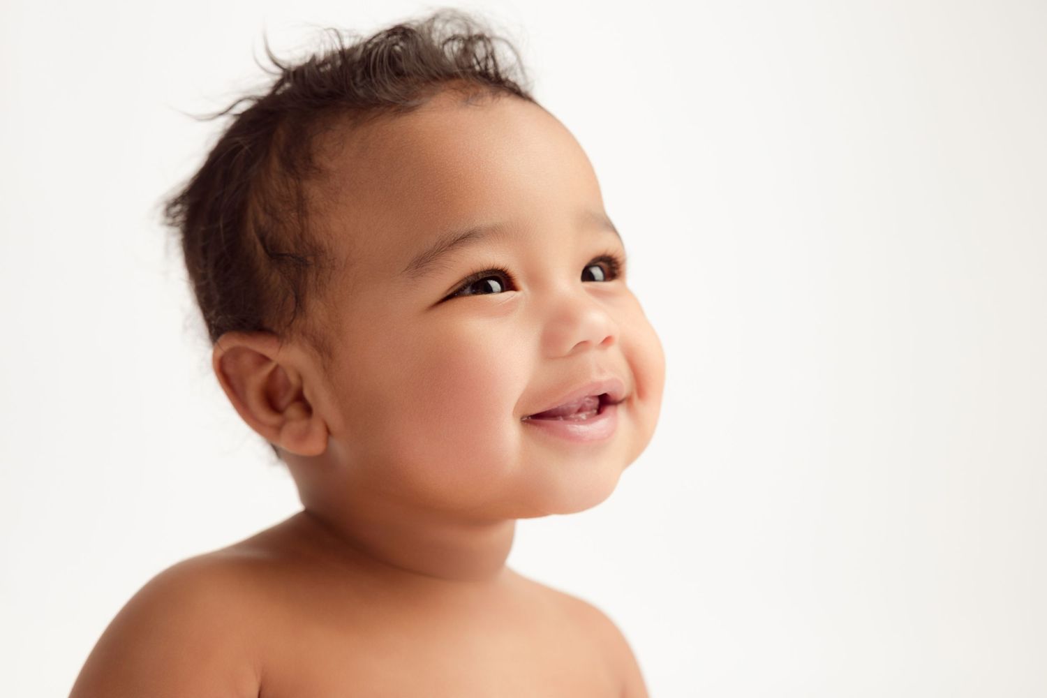 Adorable smiling baby with dark hair looking up, portrait shot on white background.