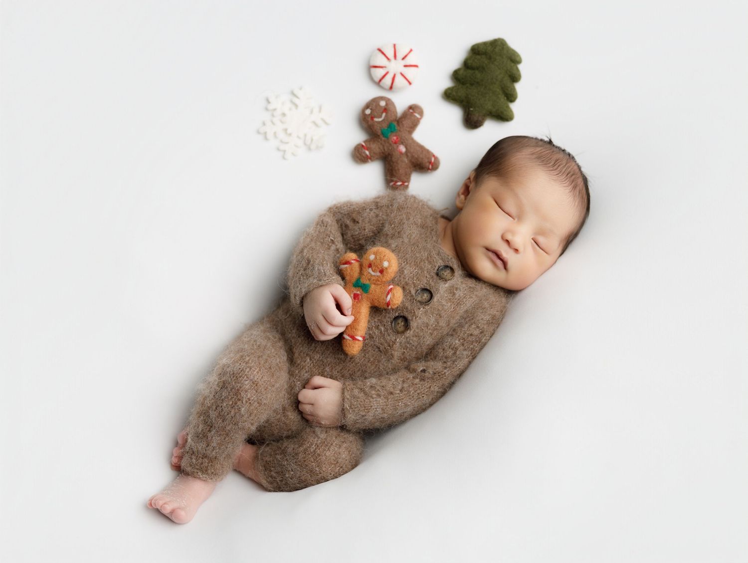 Sleeping baby in brown reindeer onesie lying on soft textured blanket with Christmas decorations.