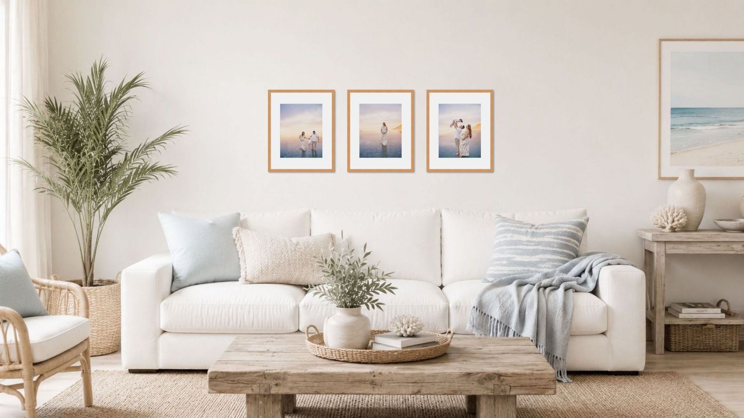 Bright coastal living room with white sofa, framed beach art, wood coffee table, and palm plant on neutral tones.