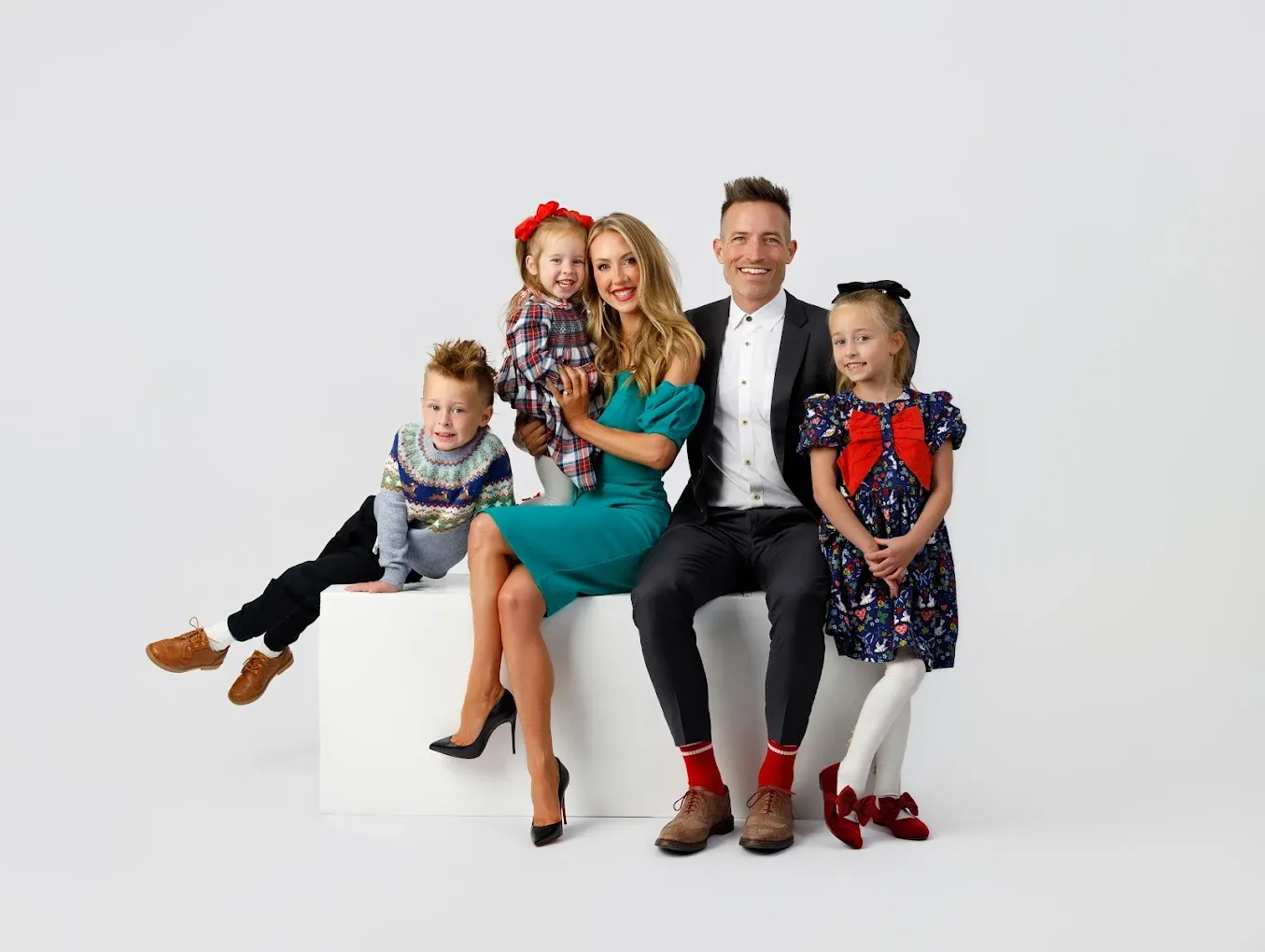 A group of people sitting together on a white bench in casual clothing for a family portrait session.
