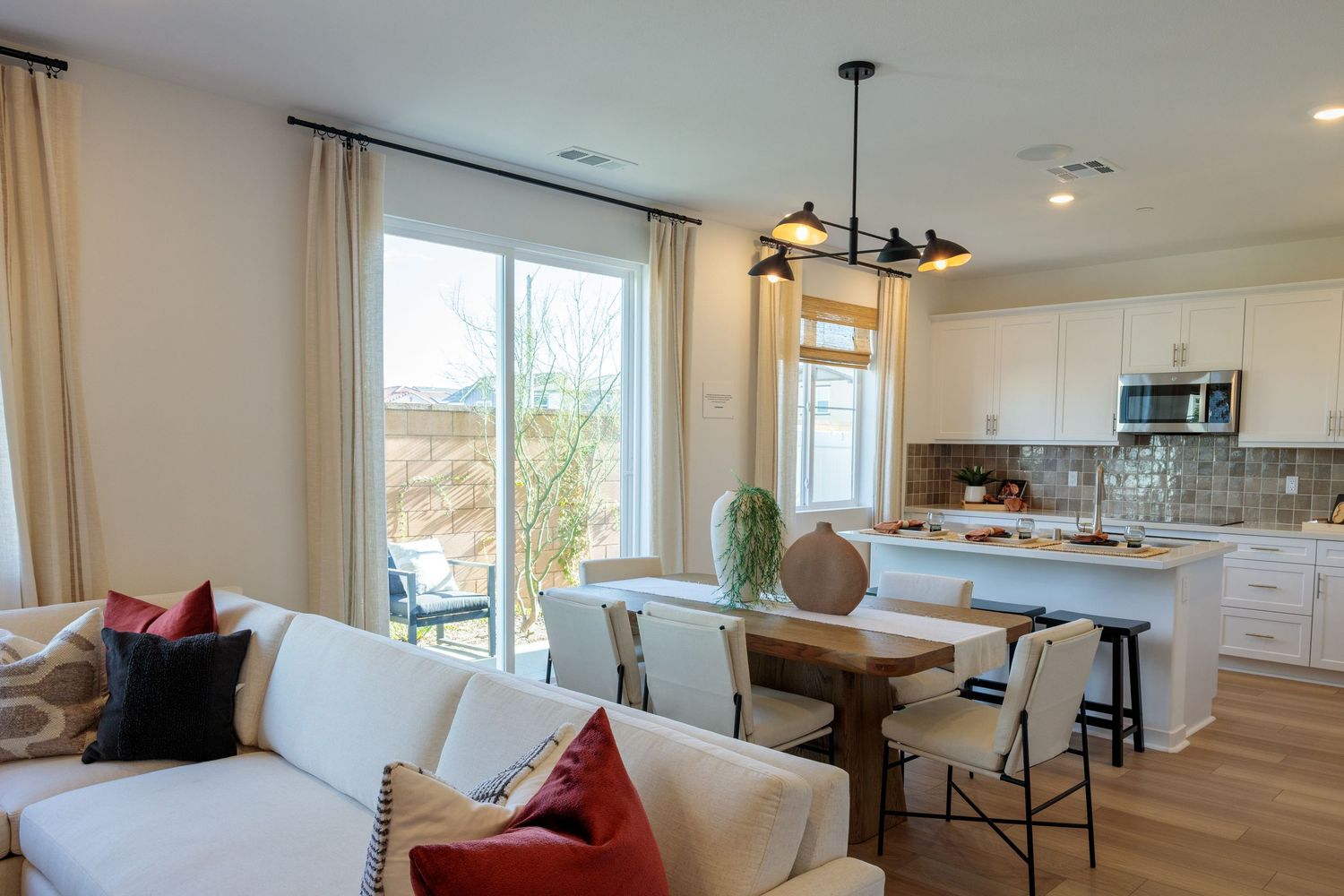 Modern open concept living room and kitchen with white walls, hardwood floors, and large windows letting in natural light.