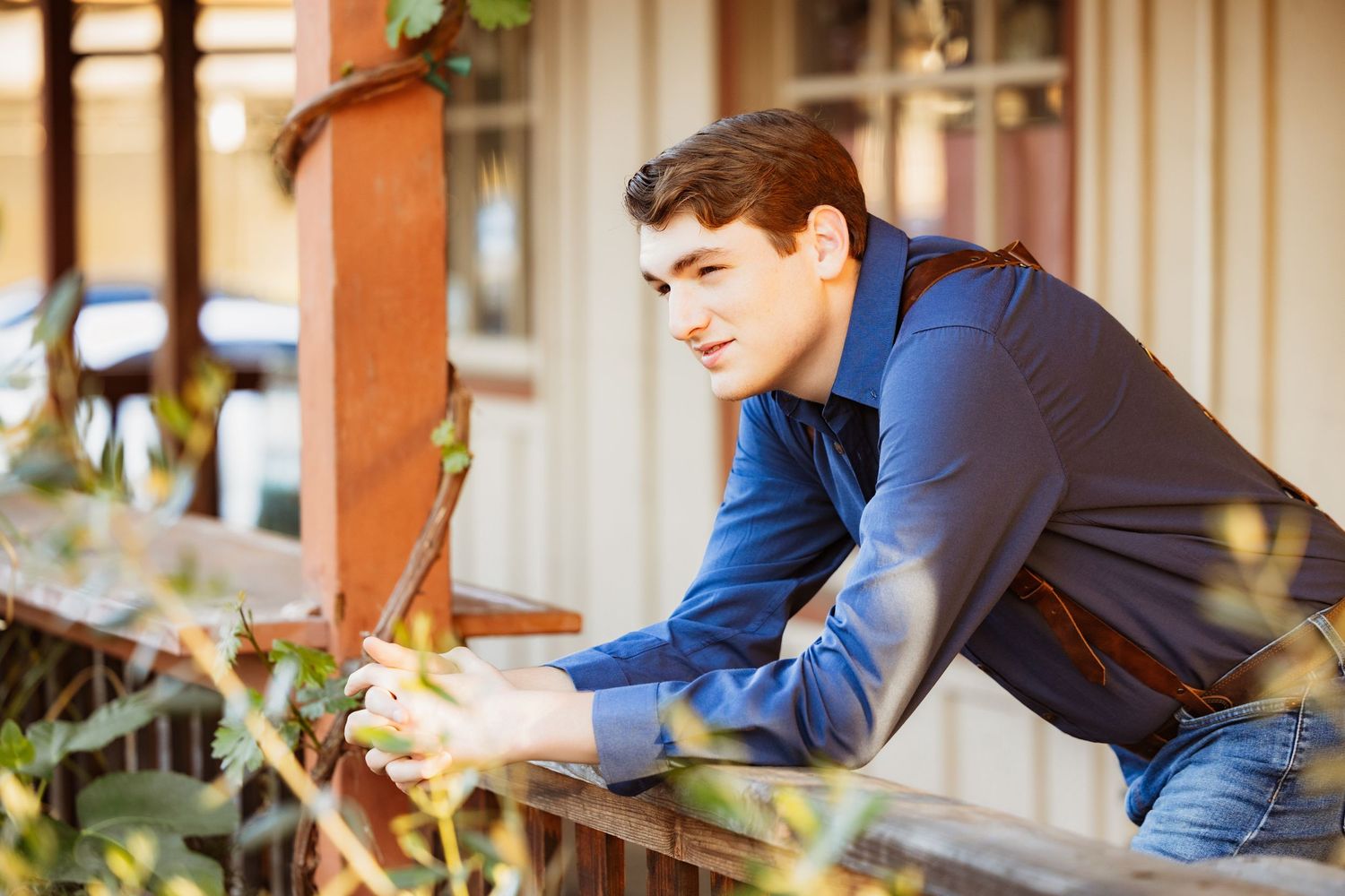 Young man in blue shirt leaning on wooden fence outdoors.