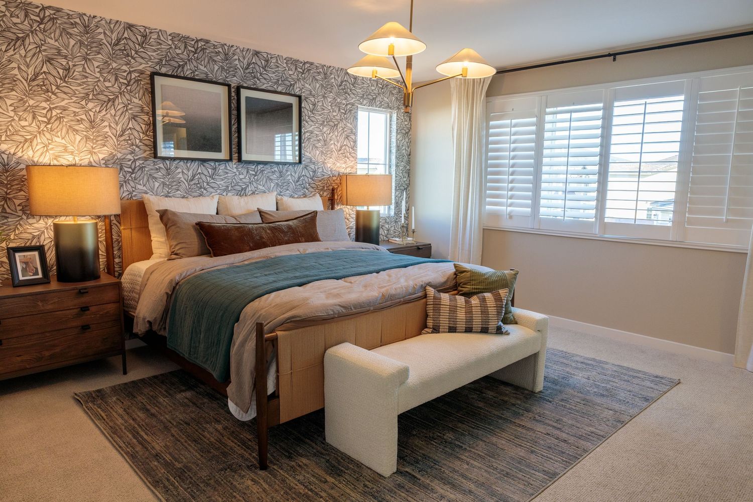 Modern bedroom interior with white bedding, warm lighting, and coastal-inspired decor features plantation shutters and area rug.
