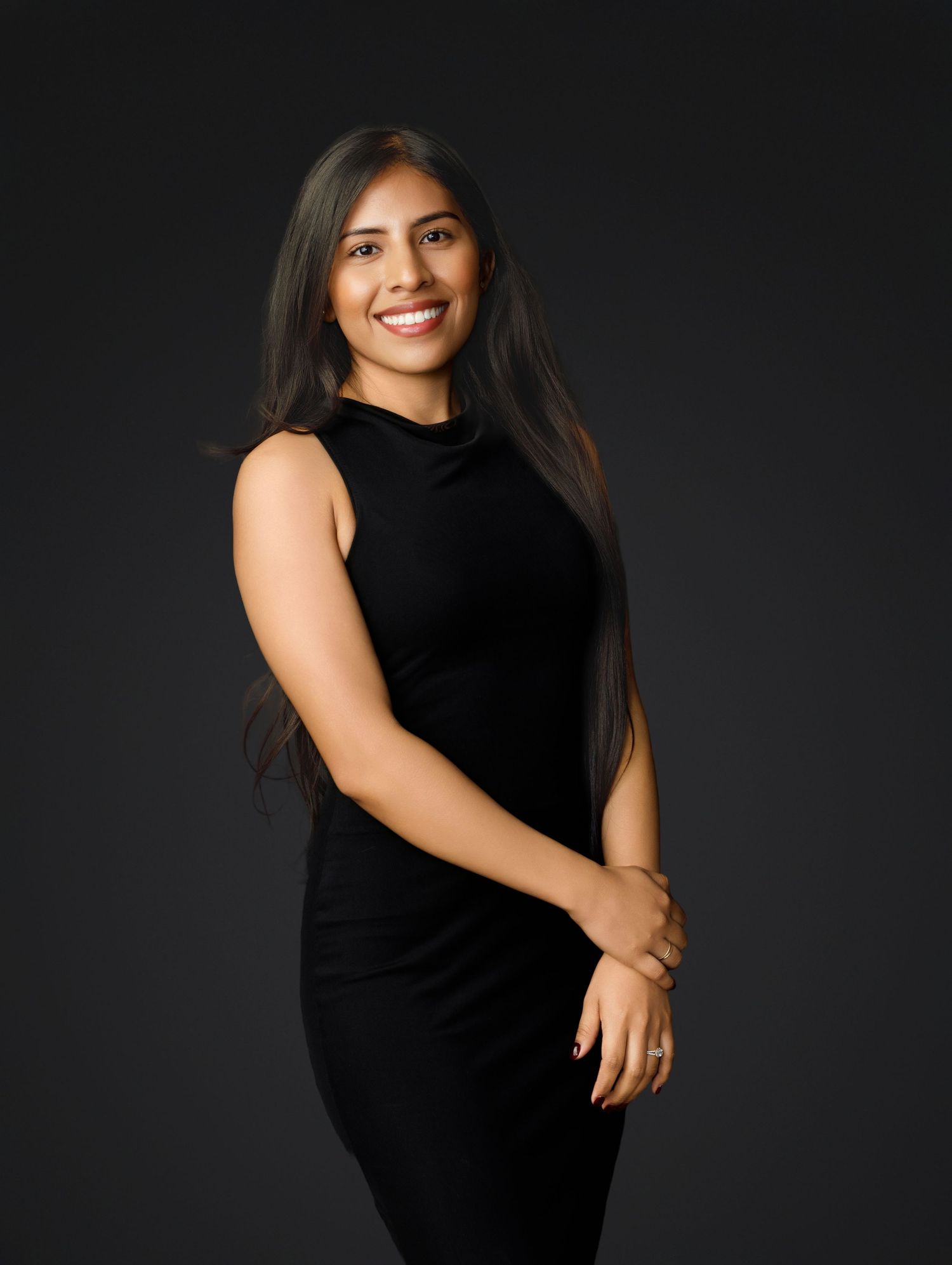 Woman in black sleeveless dress poses confidently against dark background in professional studio portraits.