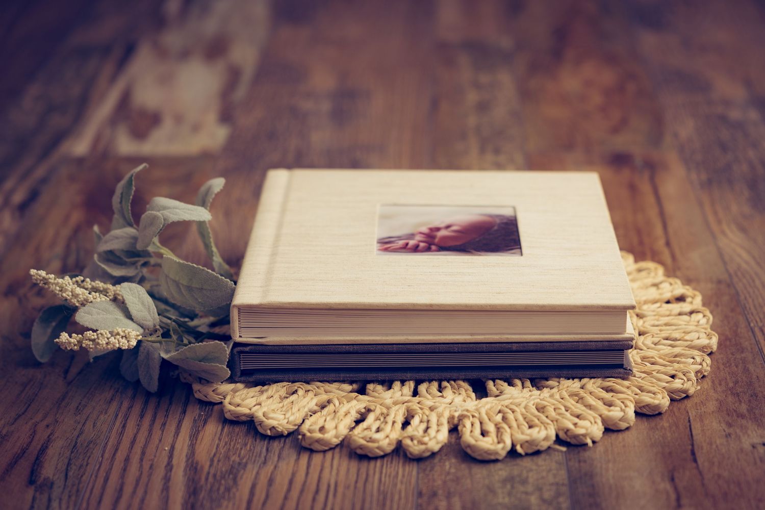 A vintage photo album rests on a crocheted doily with dried flowers on a rustic wooden table.