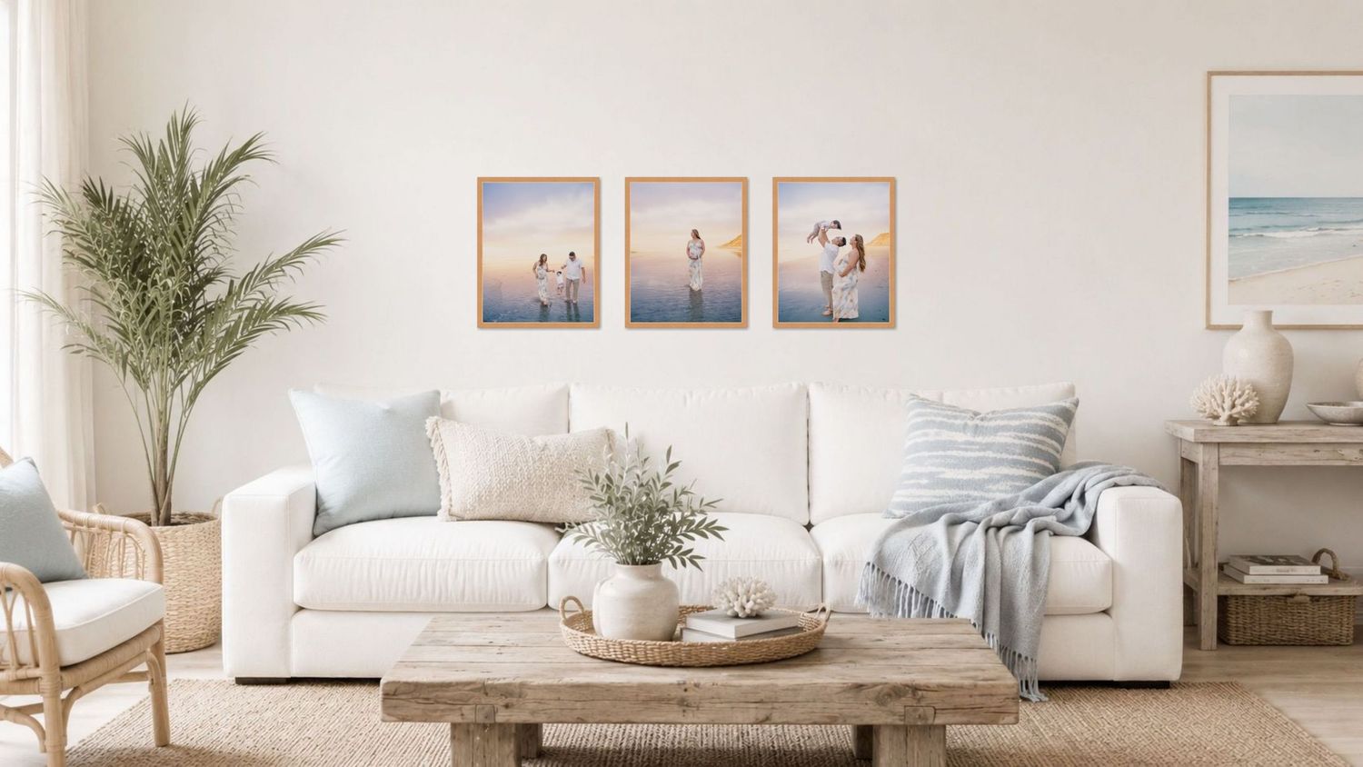 Coastal living room with white sofa, three beach-themed framed prints, wooden coffee table, and palm plant decor.