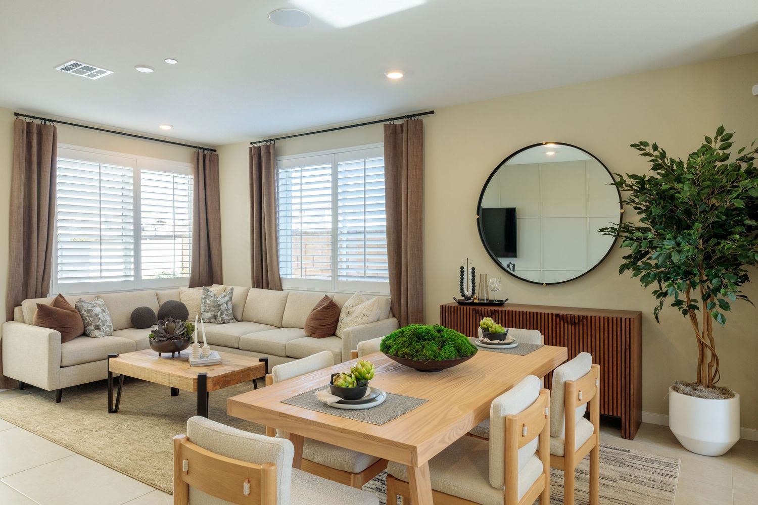 A bright and airy modern living room with white walls, beige furniture, and natural light streaming through large windows.