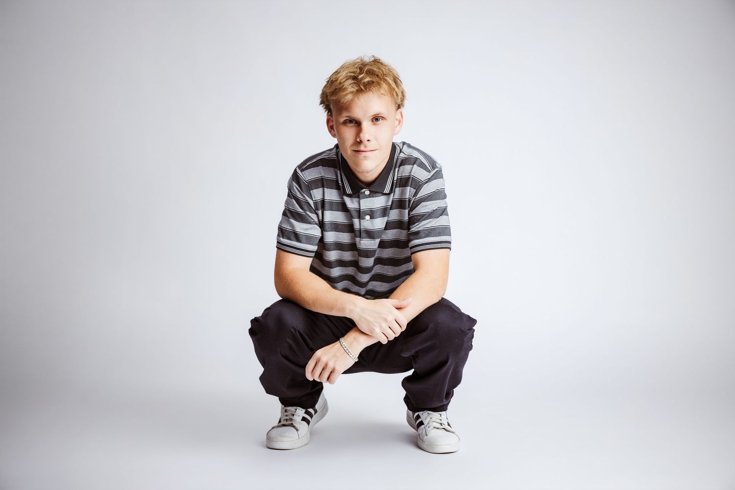 Young man in striped polo shirt crouching confidently against white background.