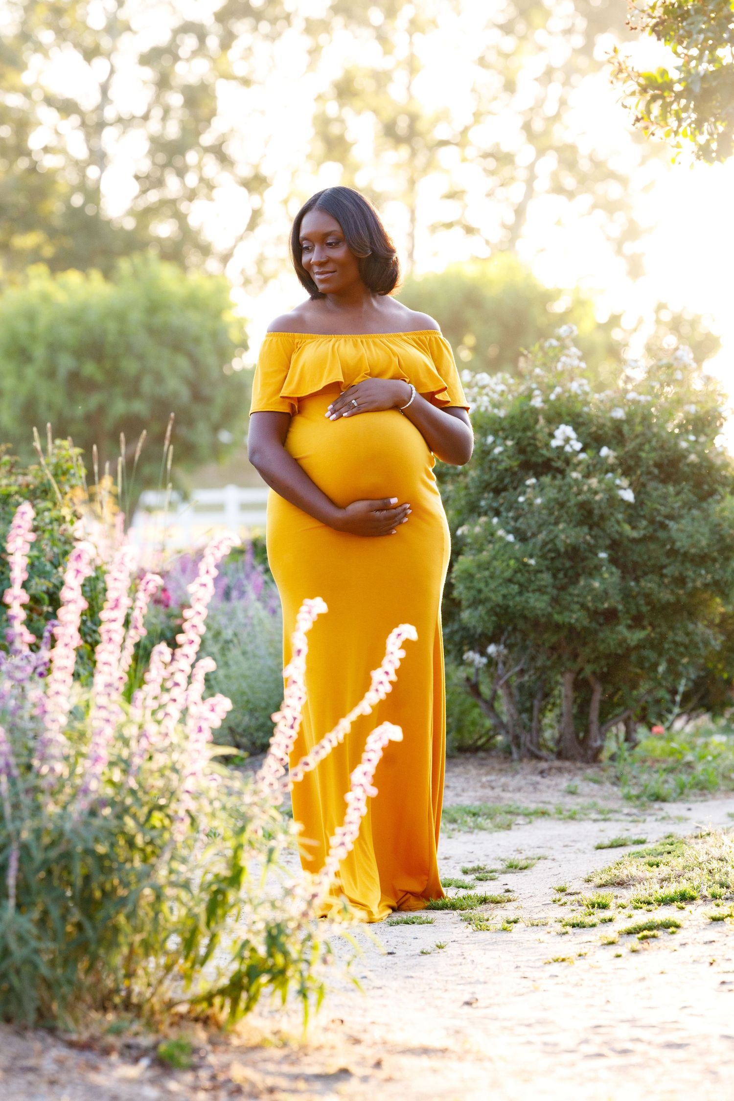 A glowing sunset maternity photoshoot in a garden with purple flowers and golden light creates a dreamy atmosphere.