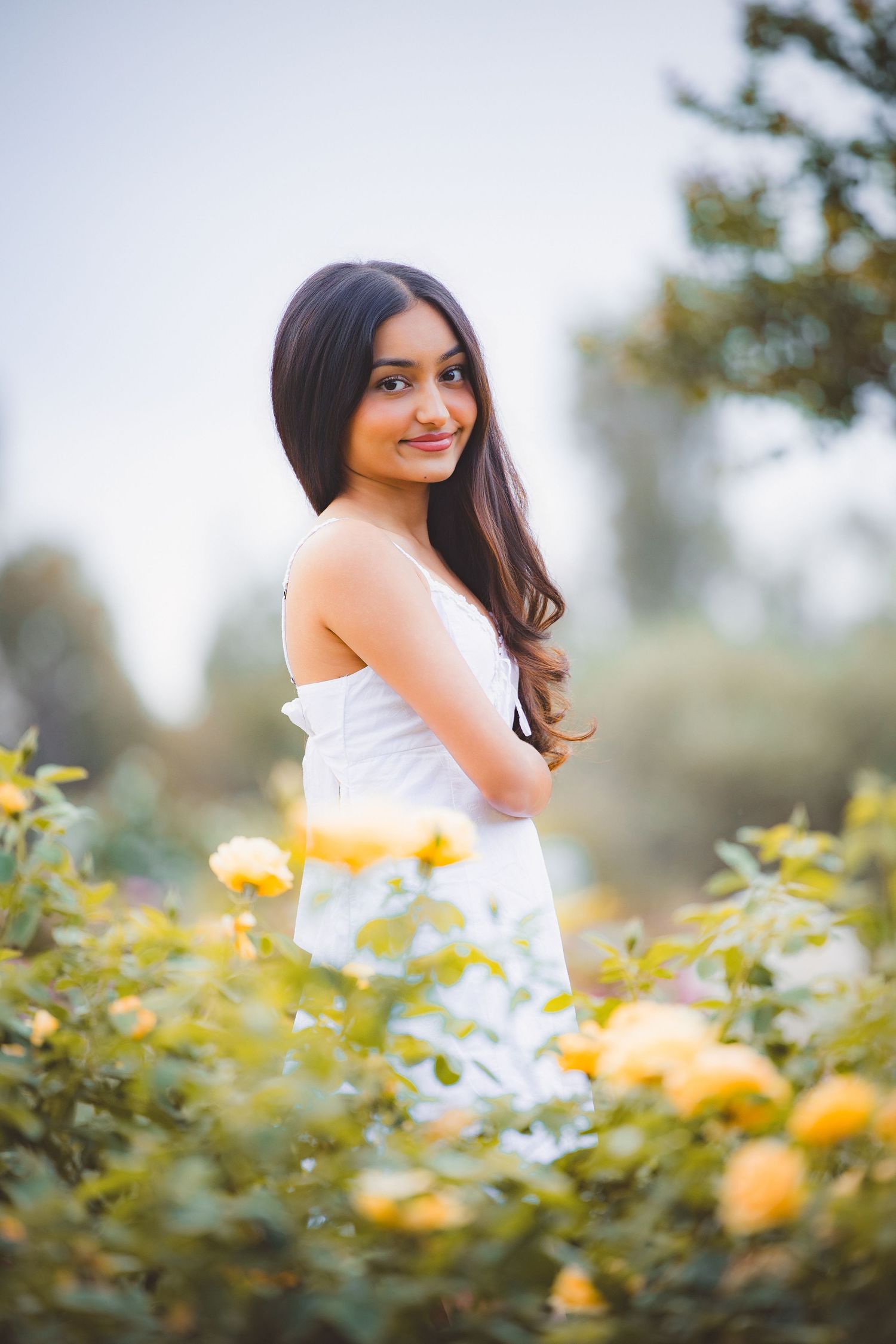 Young woman in white dress standing among yellow roses in garden.