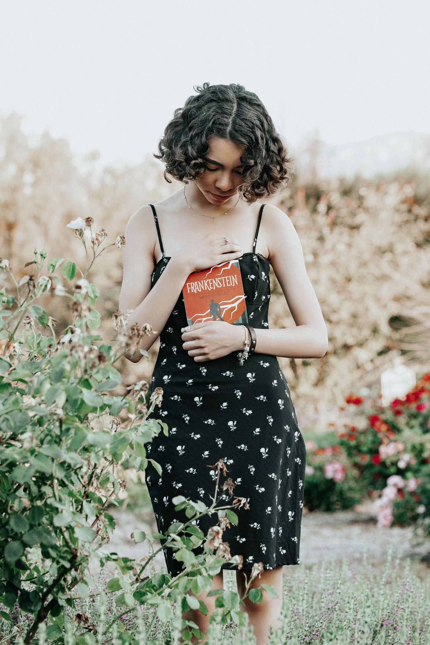 A person in a floral sundress stands in a blooming garden surrounded by delicate white flowers and greenery.