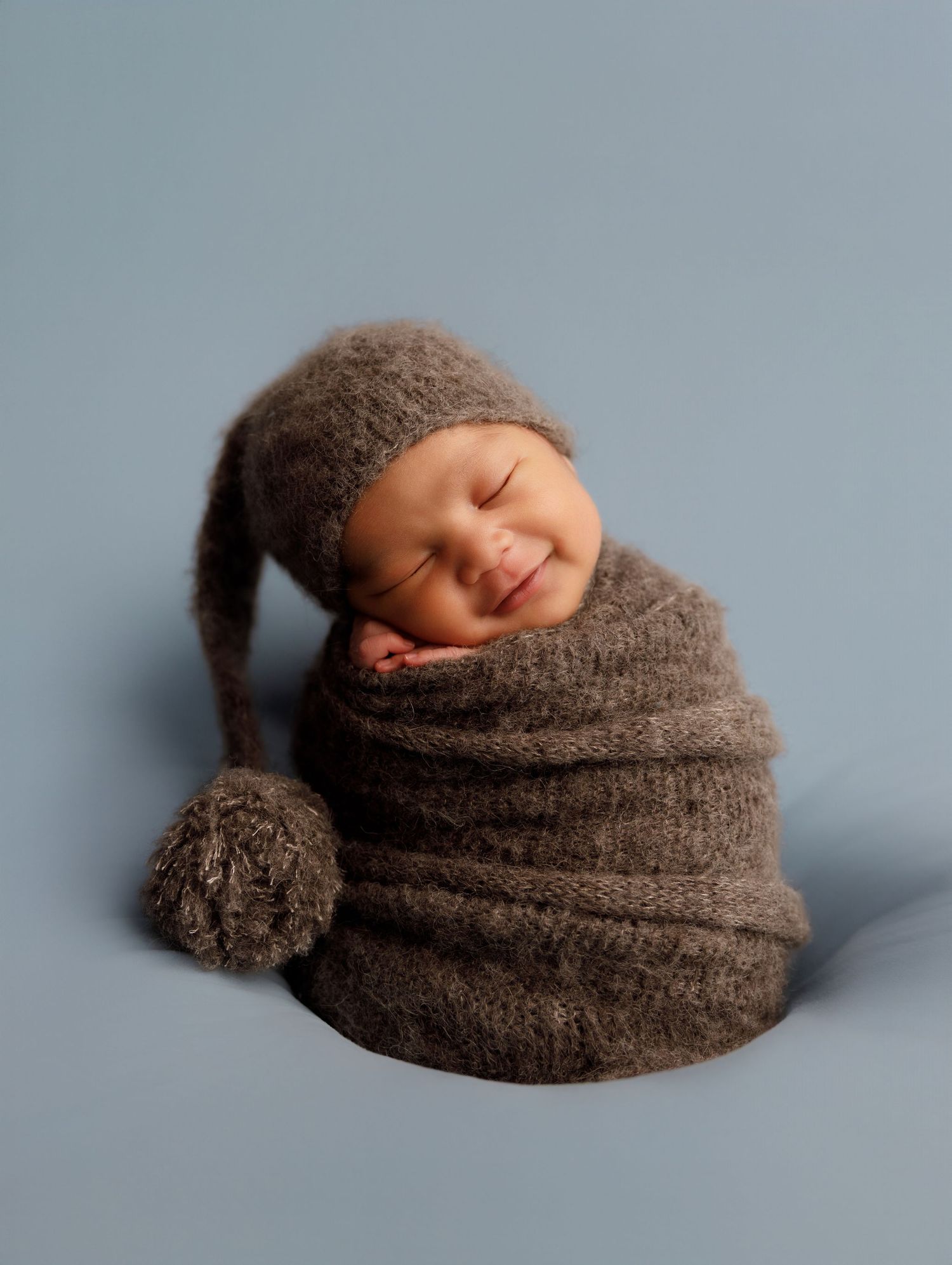 A newborn baby wrapped in a brown knit blanket photographed from different angles on a blue background.