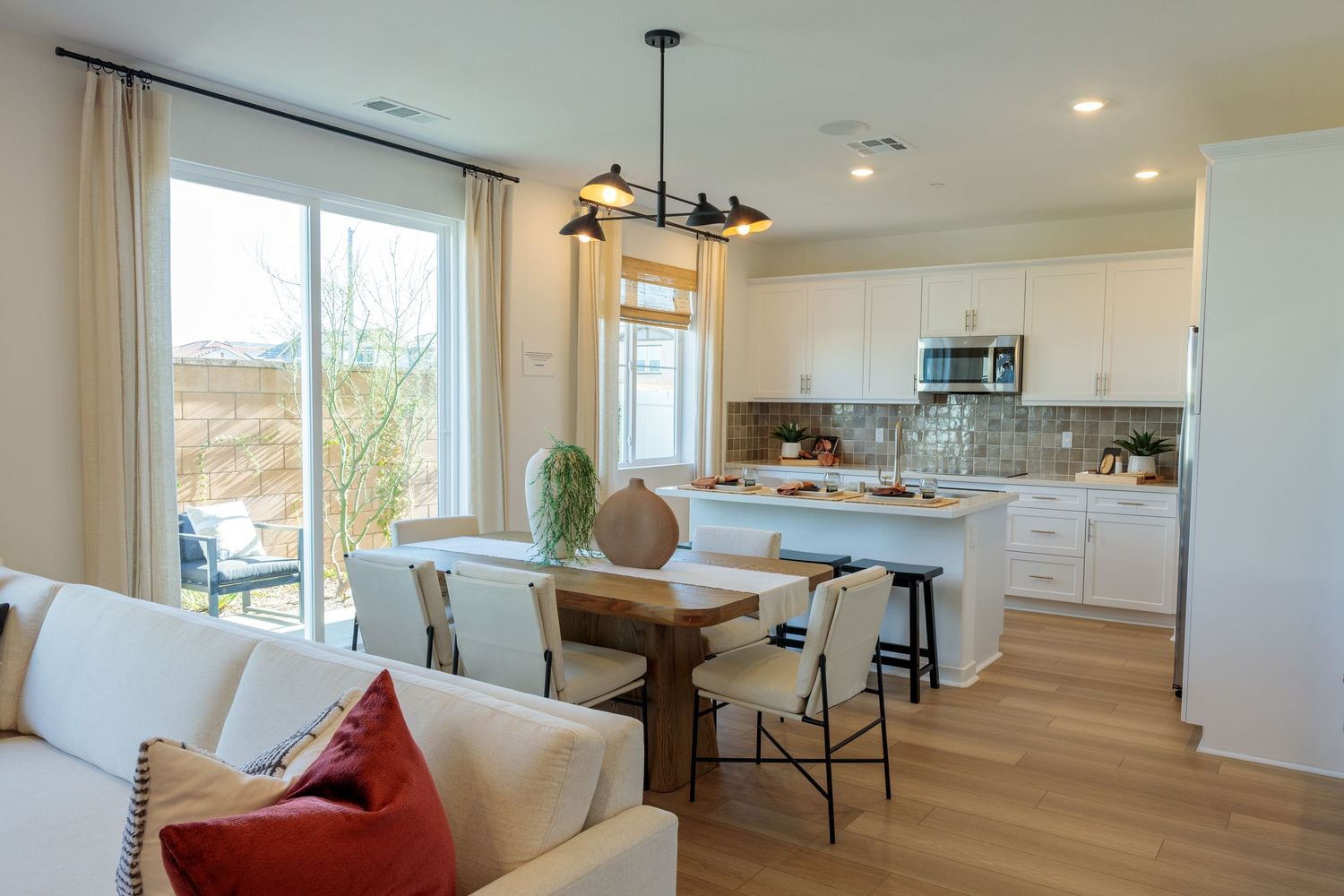 Modern open concept kitchen and living area with white cabinets, hardwood floors and large windows overlooking outdoor view.