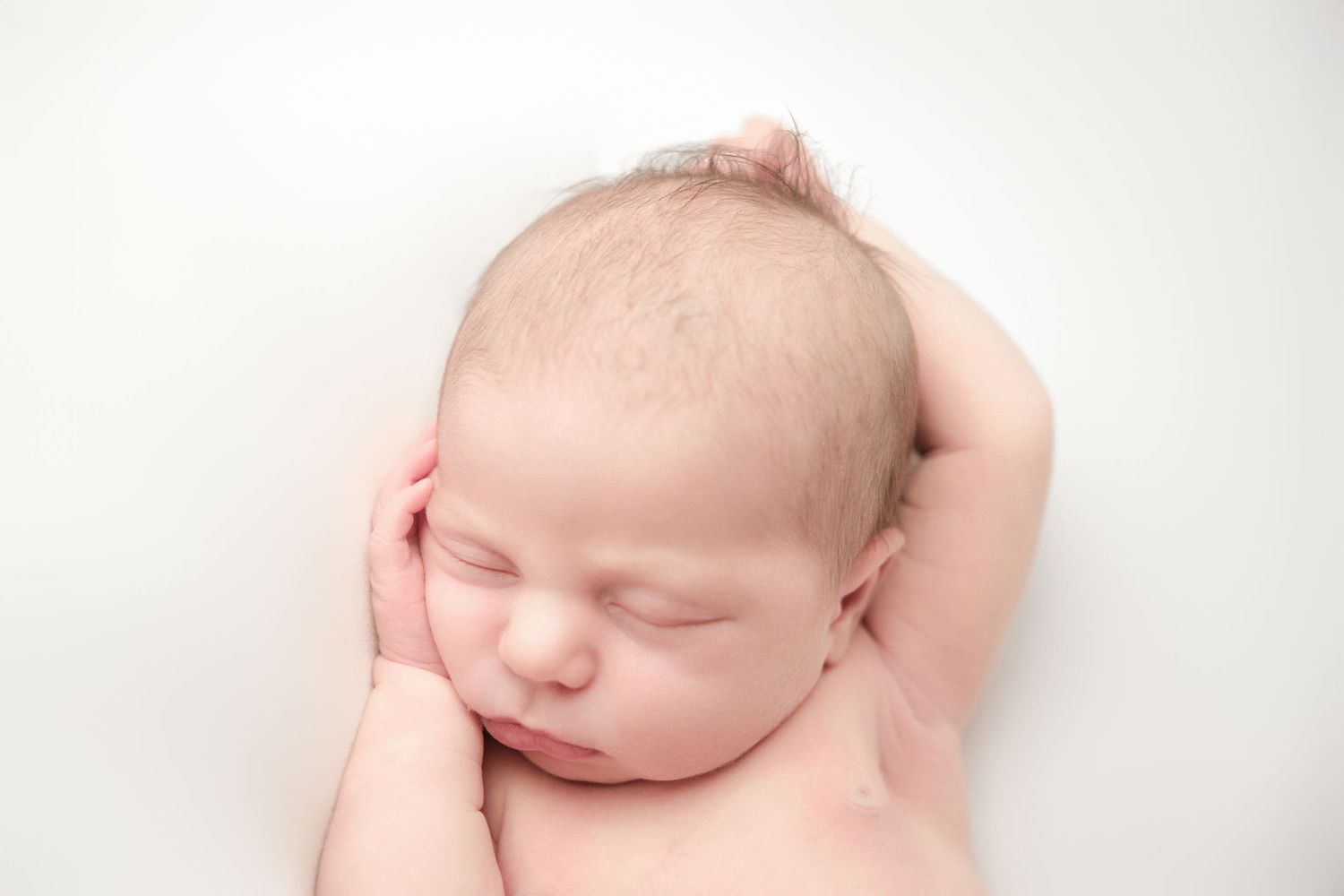 Peaceful sleeping newborn baby with delicate features rests on white backdrop in soft lighting.