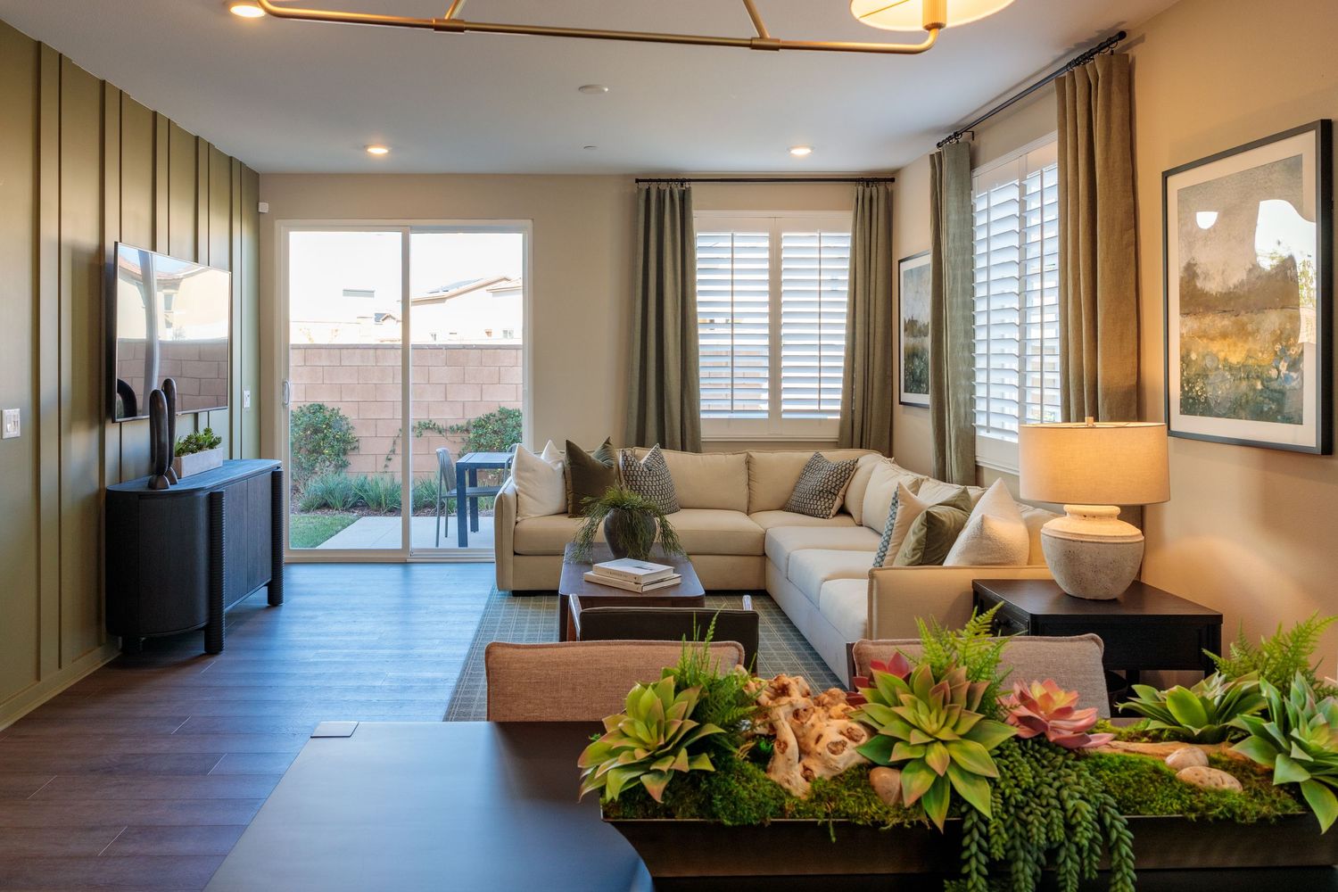 Modern living room with sectional sofa, hardwood floors, and indoor plants featuring natural light from large windows.