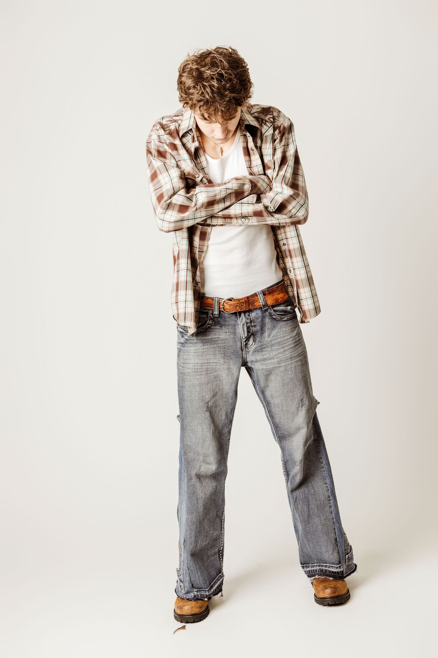 Child wearing plaid shirt and baggy jeans stands in casual poses against white backdrop in photo series.