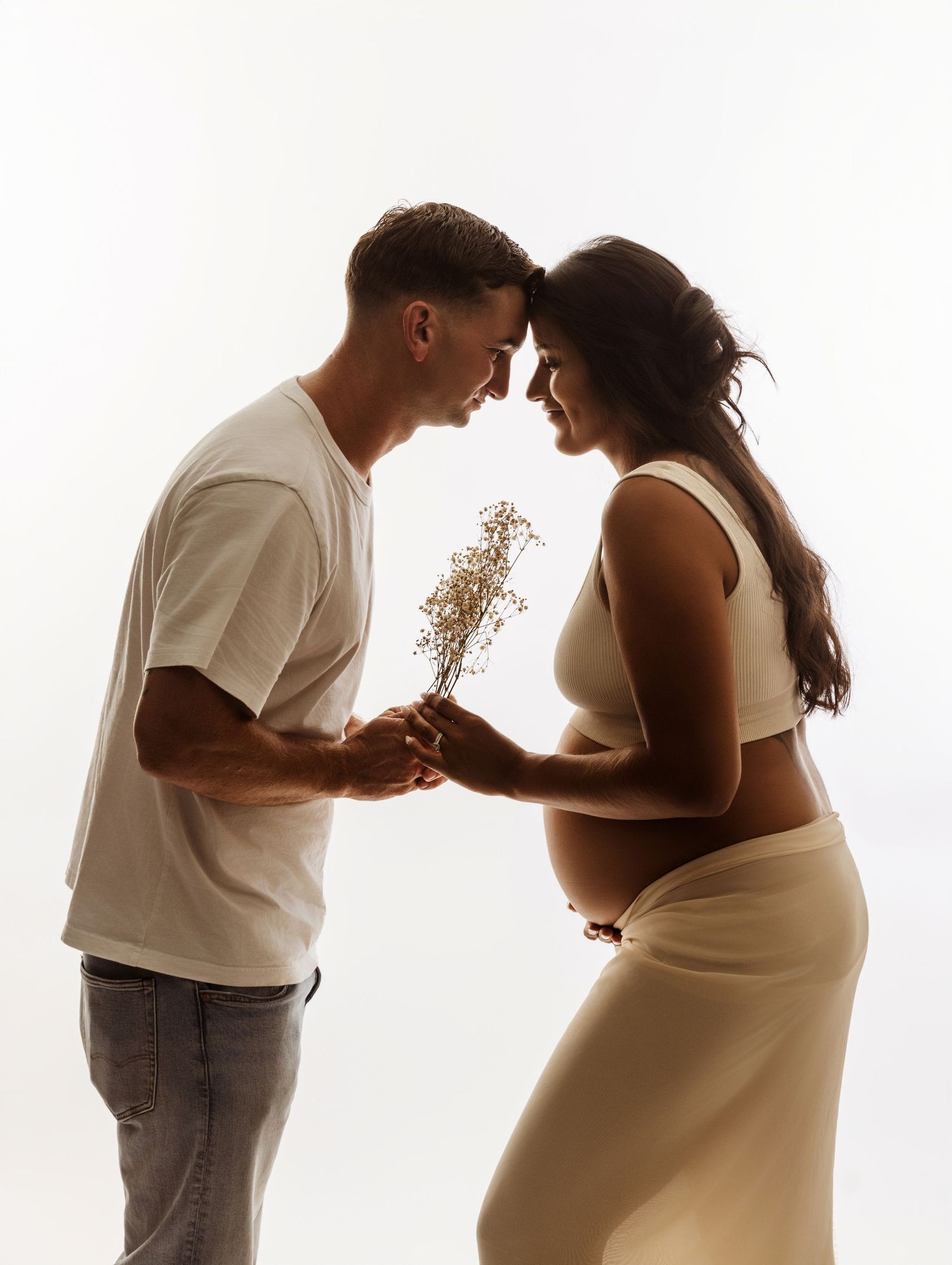 A romantic silhouette of a couple sharing a tender moment with dried flowers between them against a bright backdrop.