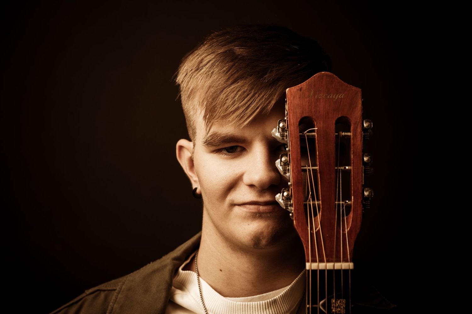 A musician poses with an acoustic guitar against a dark background in a series of similar portrait shots.