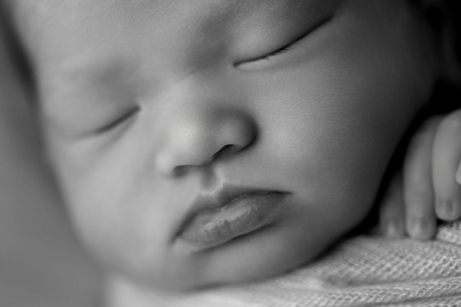 Black and white close-up photo showing a sleeping baby's peaceful face in soft focus.