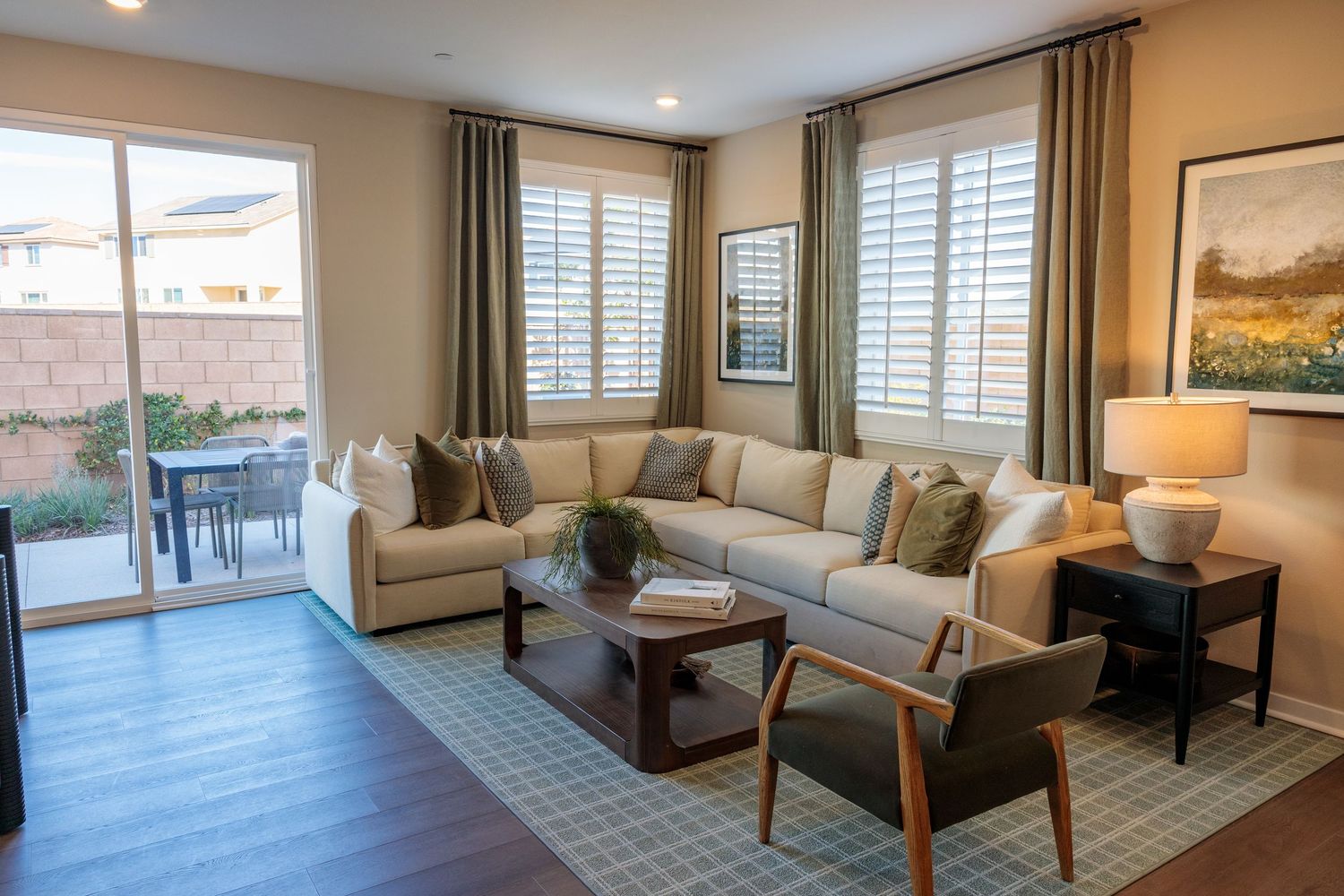 Panoramic view of a modern living room with beige walls, white shutters, and comfortable seating arrangements.