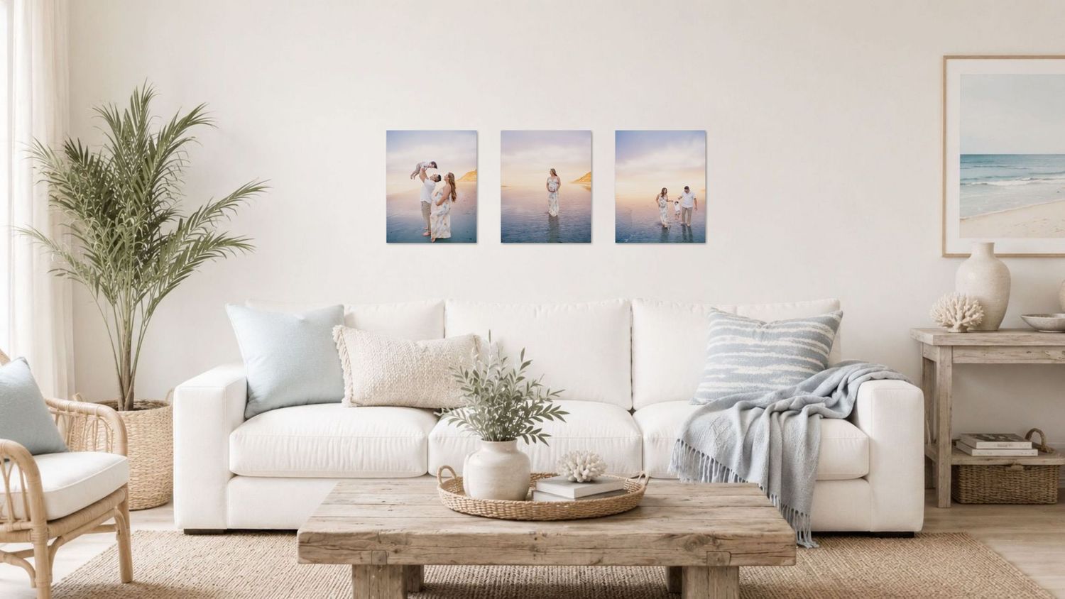 Coastal living room with white sofa, three beach artwork prints, rattan furniture, and a palm plant in soft neutral tones.