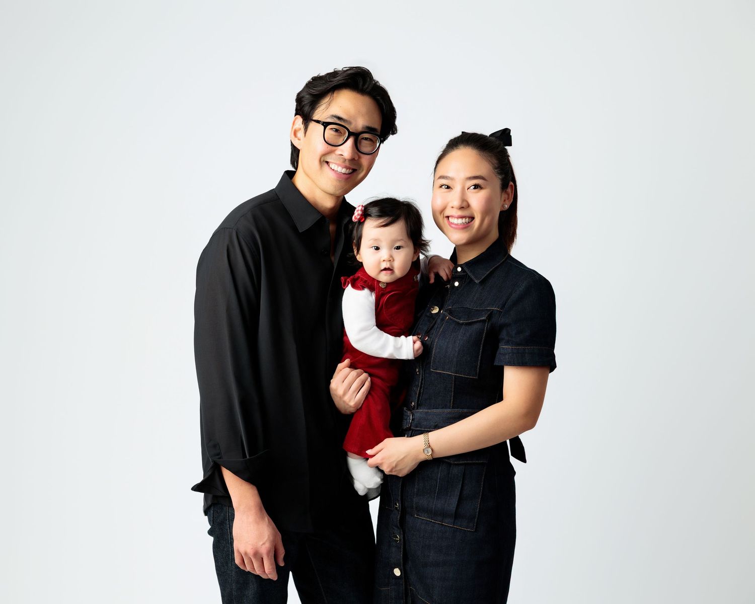 A family of three wearing black and red clothing poses together against a white background for a portrait session.