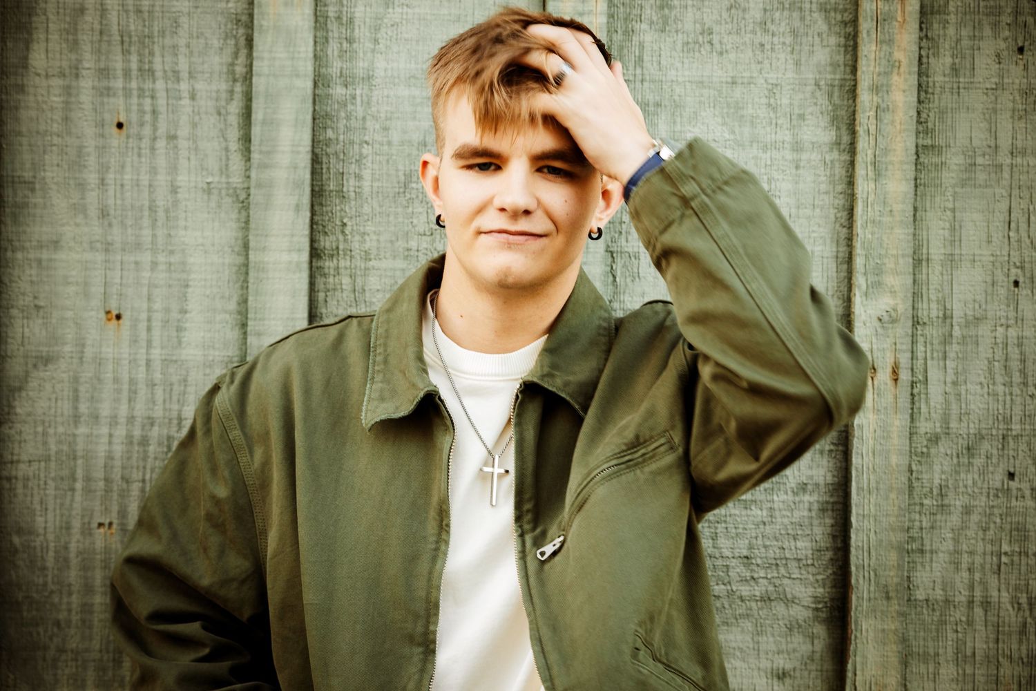 A person in an olive green jacket poses against a wooden fence background in multiple casual poses.