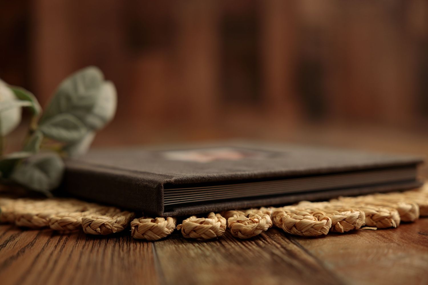 Close-up view of a dark leather photo album on wooden surface with decorative greenery and prints.
