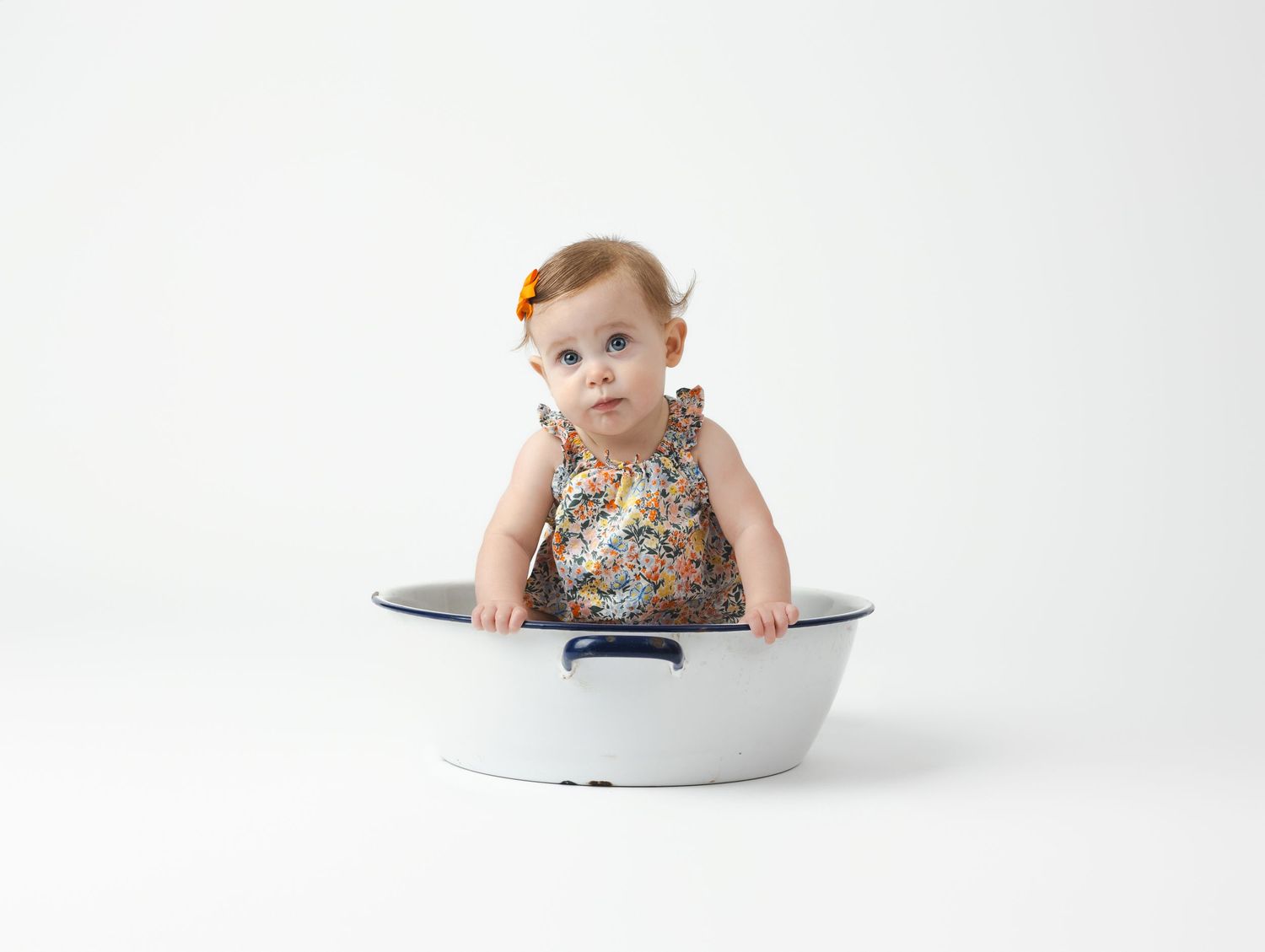 Baby in white bathtub looking playfully at camera with inquisitive expression.