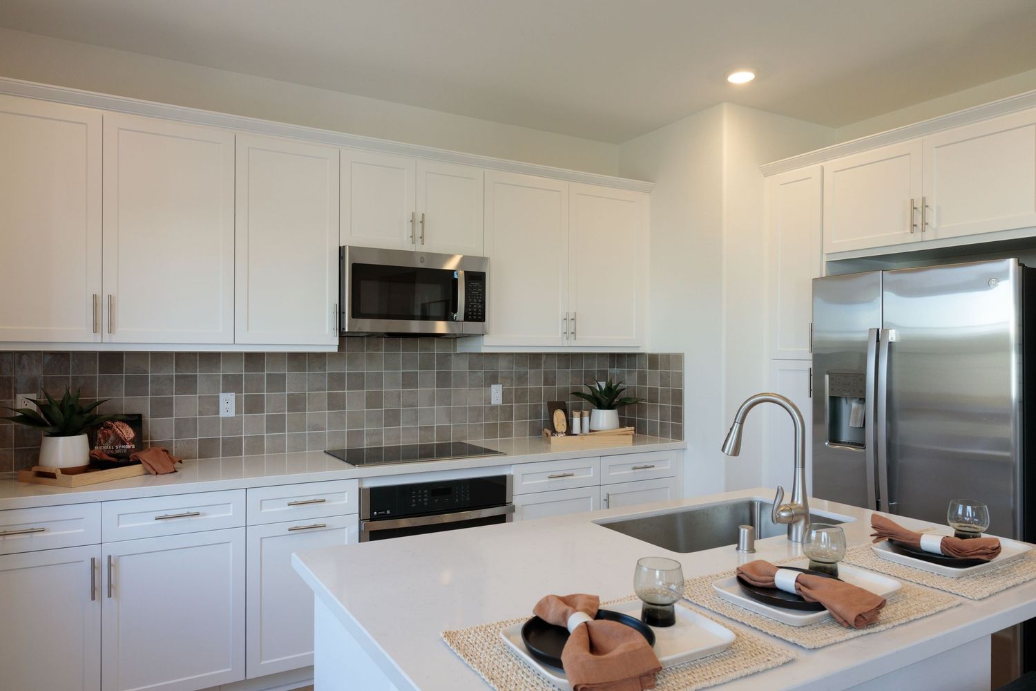Modern white kitchen with quartz countertops, stainless steel appliances, and gray tile backsplash features sleek cabinetry.