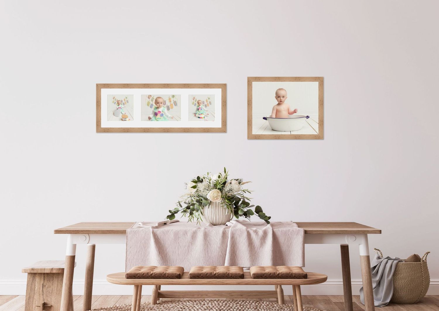 Minimalist dining room with wooden table, bench, and two framed baby photos on white wall above floral centerpiece.