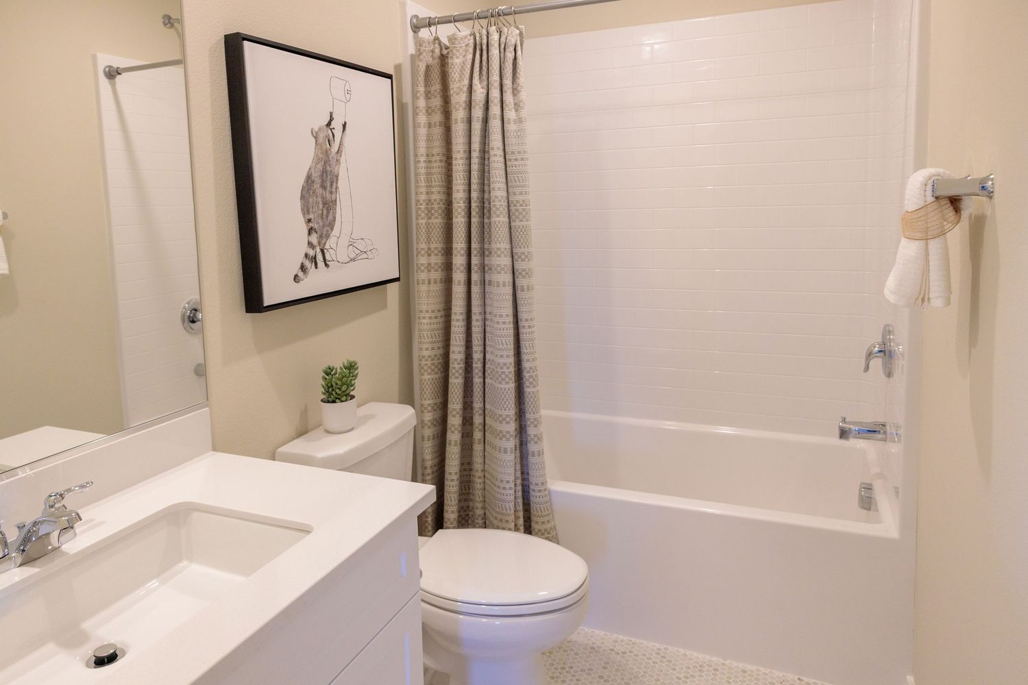 Clean white bathroom interior with striped shower curtain, bathtub, toilet and framed wall art above vanity.
