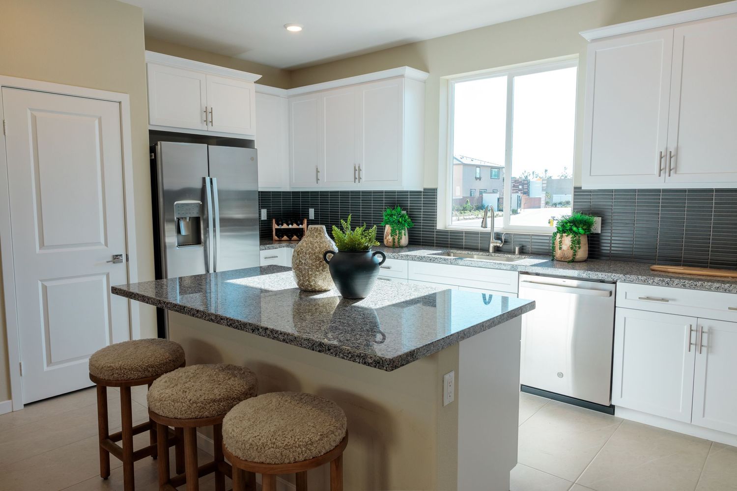 Modern white kitchen with dark granite countertops, stainless steel appliances, and brown bar stools at the island.