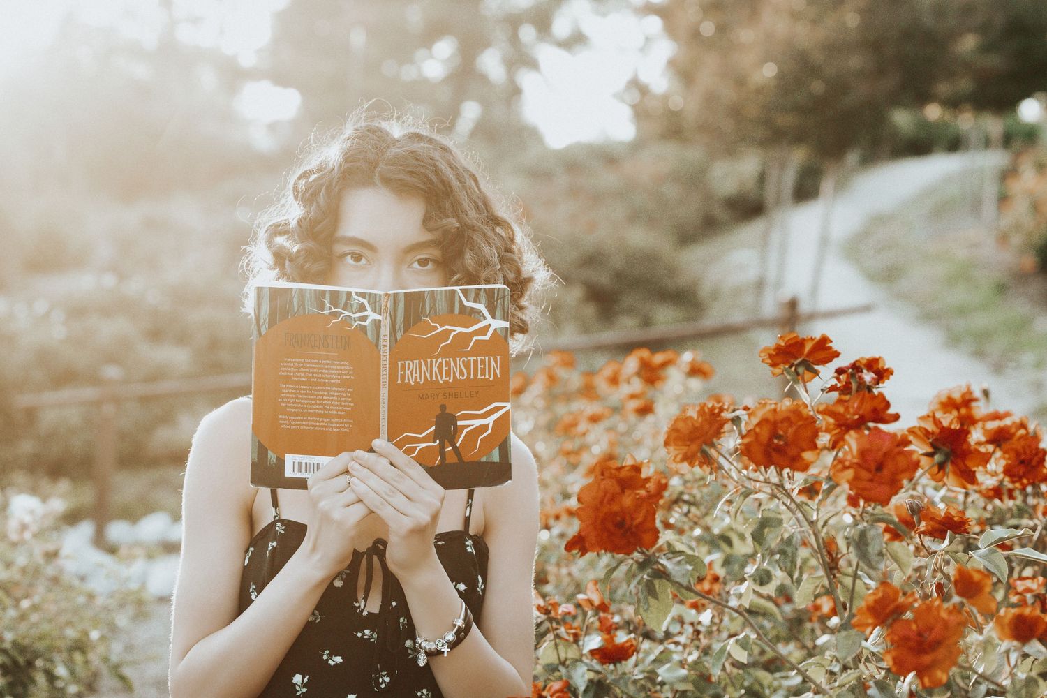 Person reading book outdoors among vibrant orange flowers in a dreamy autumn garden setting.