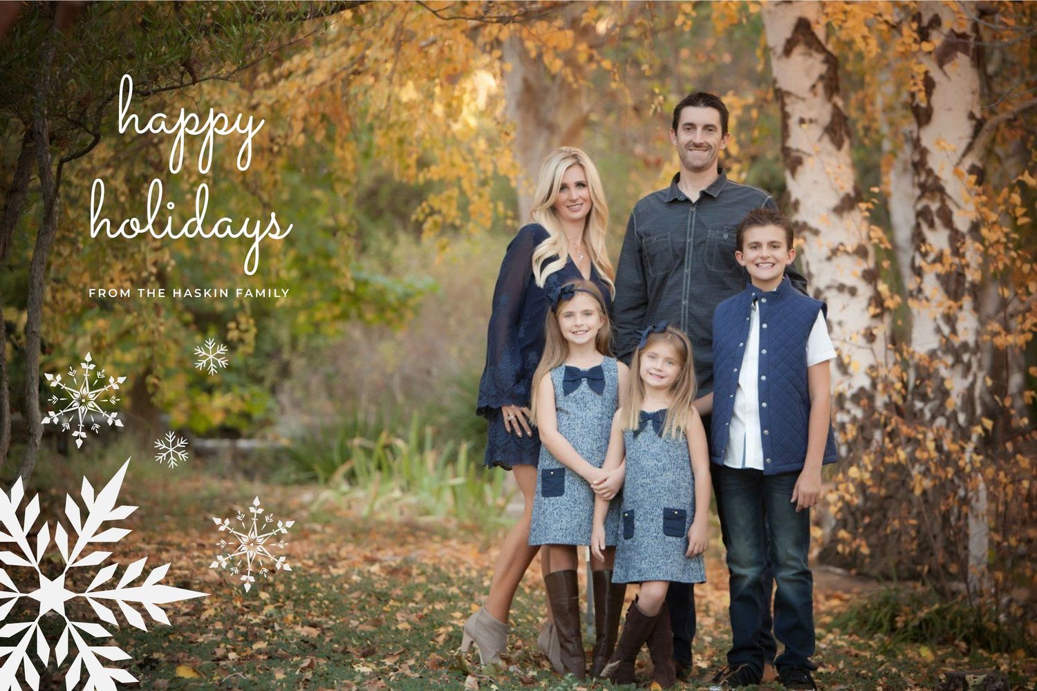 A family wearing coordinated denim and navy outfits poses together in a fall setting with autumn foliage.
