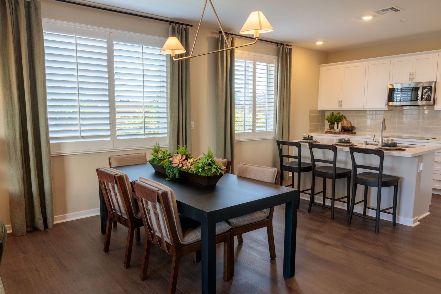 Modern dining room with dark wood table, green curtains, and pendant lighting in an open concept space.