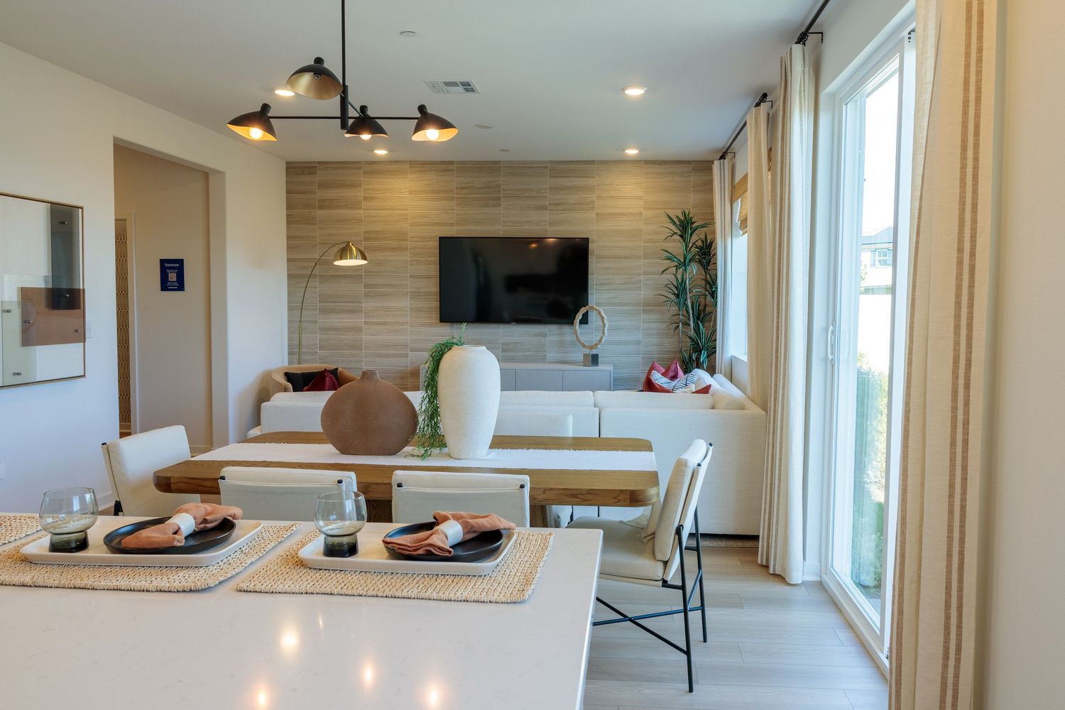Modern open concept living room with wood paneled walls, pendant lighting, and large windows offering natural light.