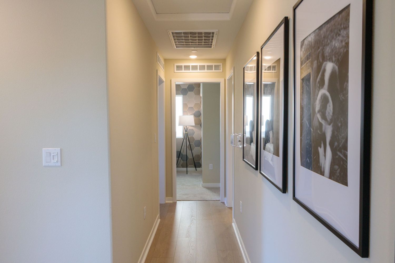 Long hallway with framed black and white photographs mounted on beige walls and recessed ceiling lights.