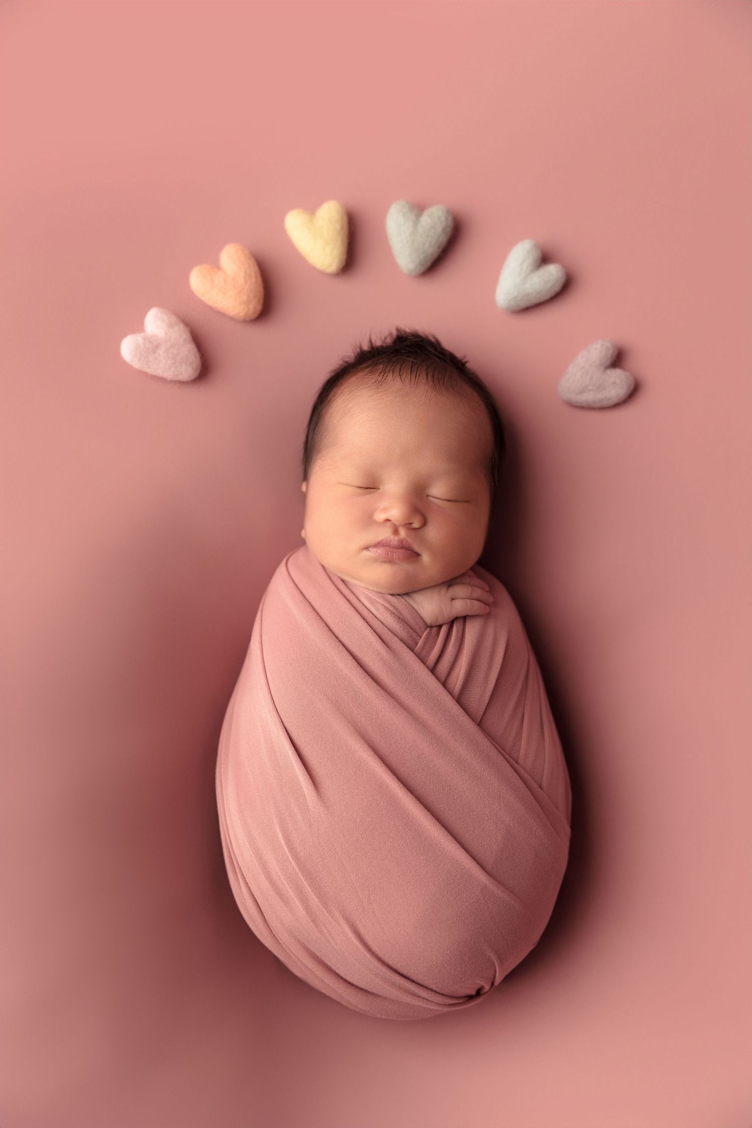 Newborn photography collage showing baby swaddled in pink fabric on pink backdrop with small heart decorations.