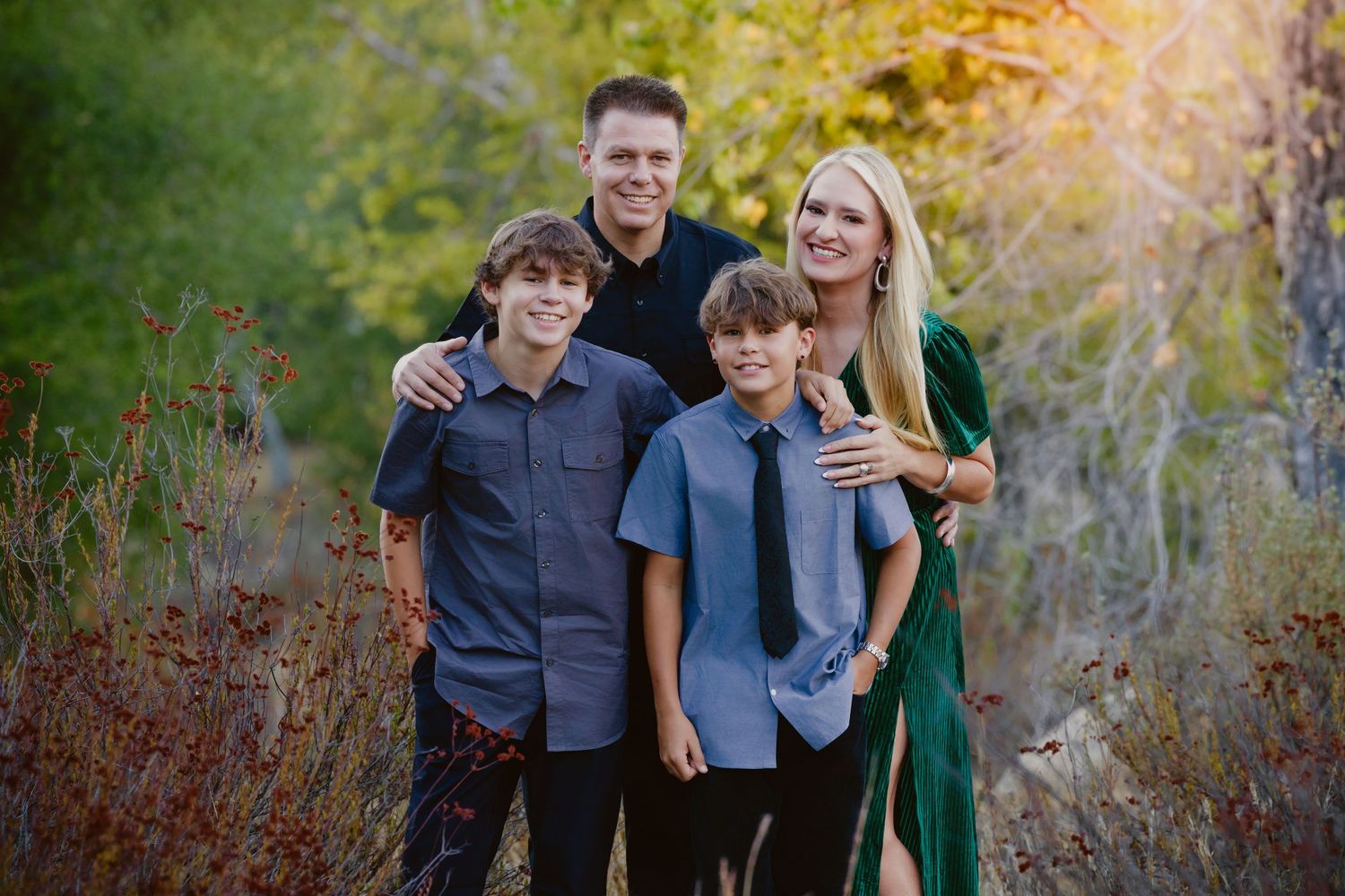 Smiling family of four, a man, woman and two boys, posing outdoors in an autumn forest for a professional family portrait.