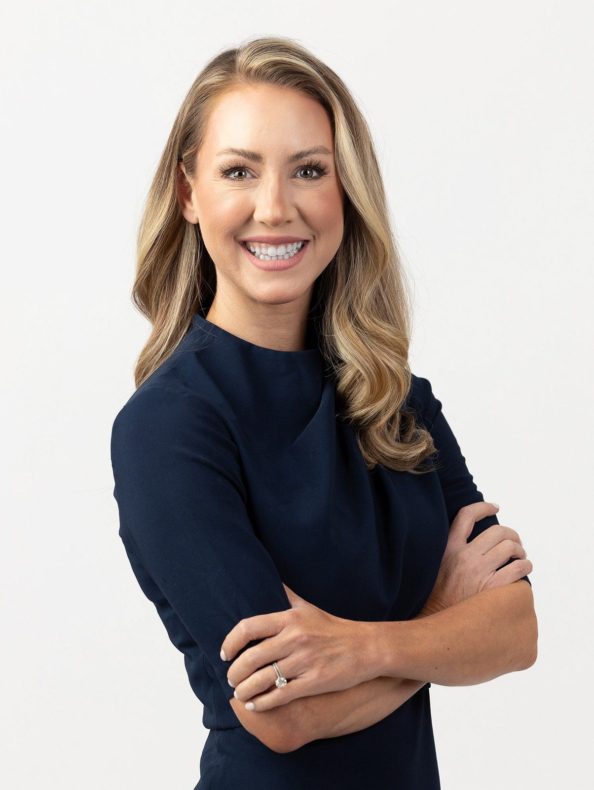 Professional woman in navy dress smiling with arms crossed against white background.