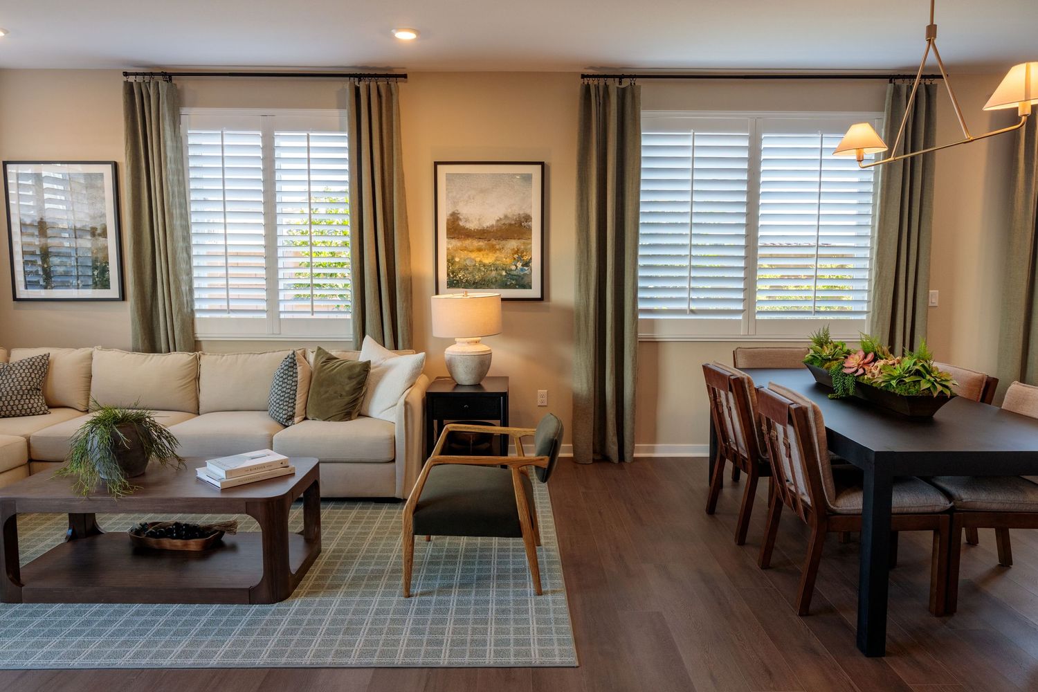 Modern open concept living space with white shutters, hardwood floors, and pendant lighting over a dining area.