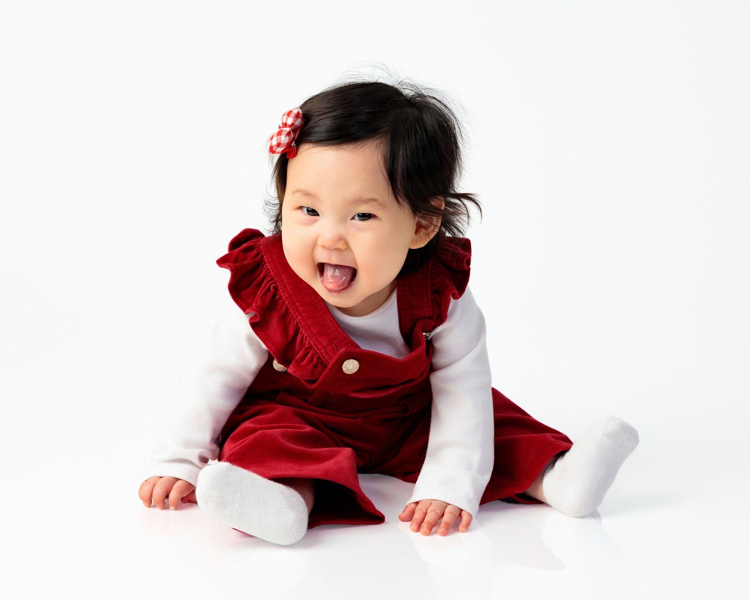 Baby in red velvet holiday dress crawls on white background in three sequential poses.