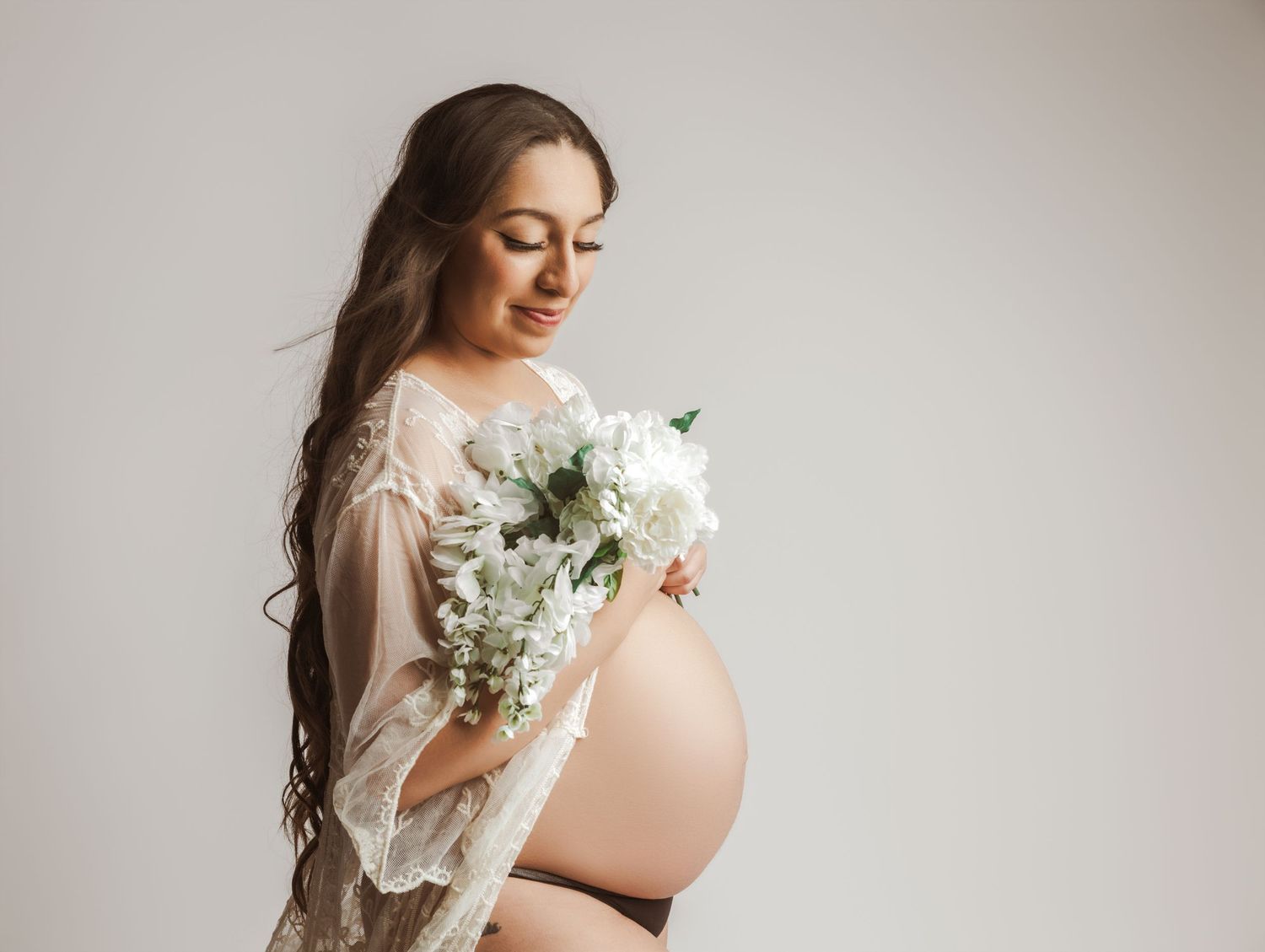 A series of soft, ethereal maternity photos featuring a woman in a white dress holding delicate white flowers.