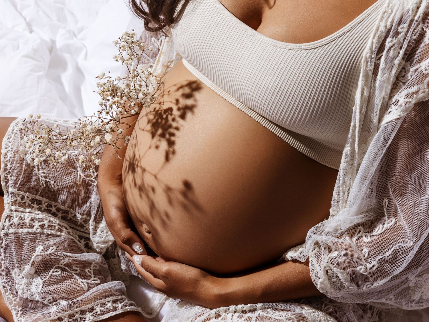 Beautiful maternity photo showing a pregnant belly with delicate shadow patterns and white lace details.